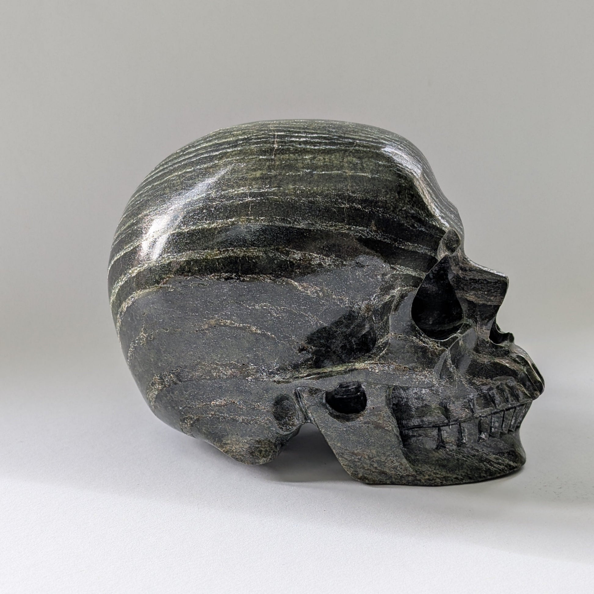 Ein monumentaler, 1204g schwerer Kristallschädel 'Scryer' aus dunkelgrünem Serpentin mit hypnotisierendem, silbrigem Schimmer.