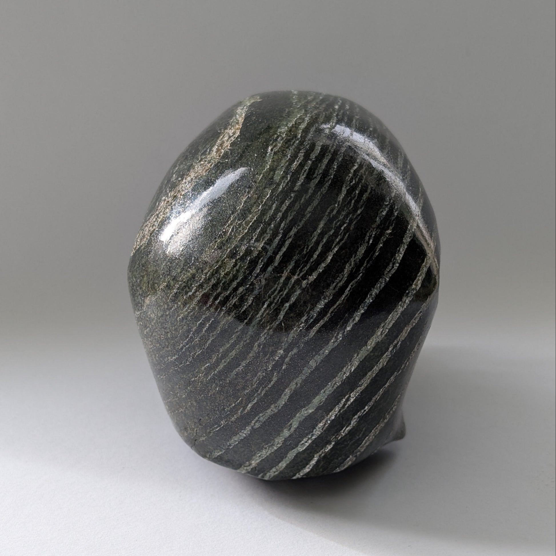 Ein monumentaler, 1204g schwerer Kristallschädel 'Scryer' aus dunkelgrünem Serpentin mit hypnotisierendem, silbrigem Schimmer.