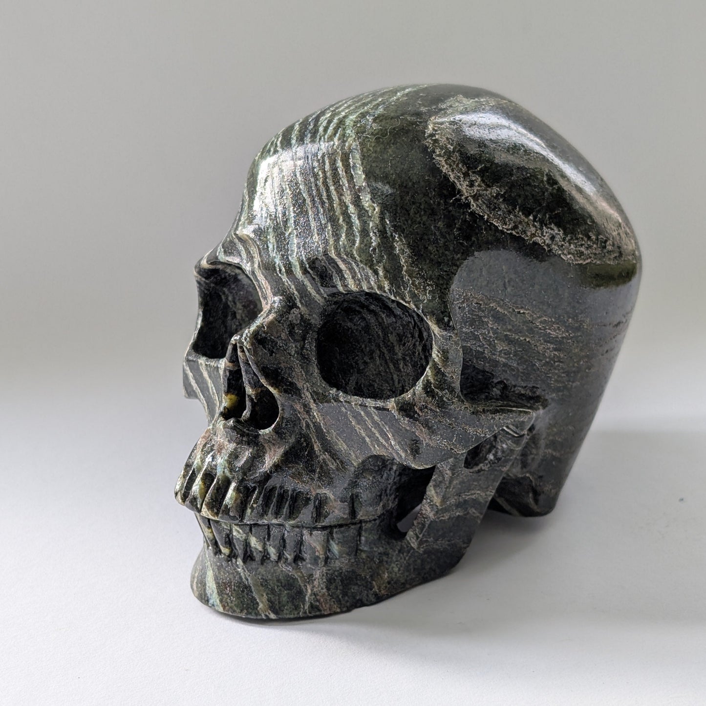 Ein monumentaler, 1204g schwerer Kristallschädel 'Scryer' aus dunkelgrünem Serpentin mit hypnotisierendem, silbrigem Schimmer.