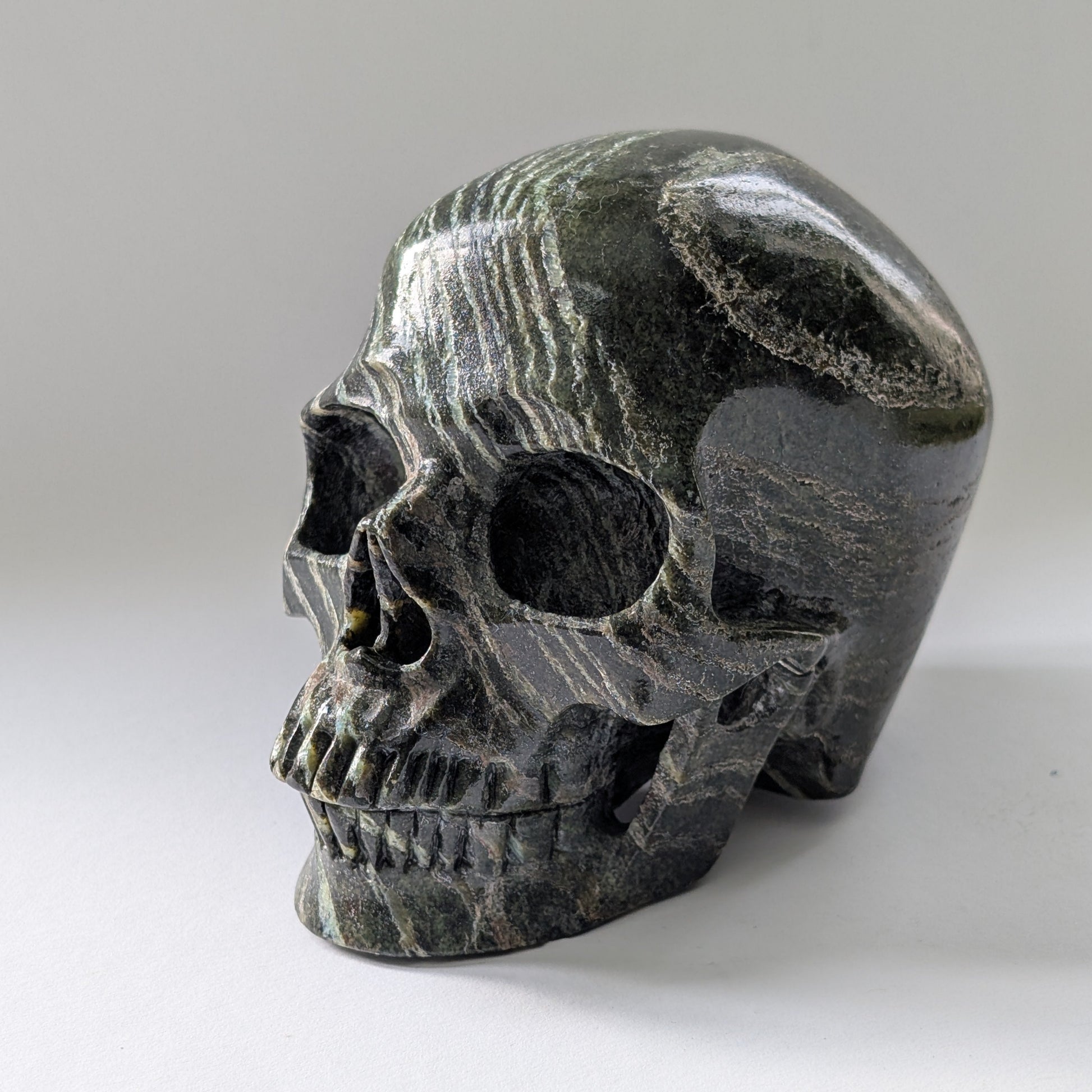 Ein monumentaler, 1204g schwerer Kristallschädel 'Scryer' aus dunkelgrünem Serpentin mit hypnotisierendem, silbrigem Schimmer.