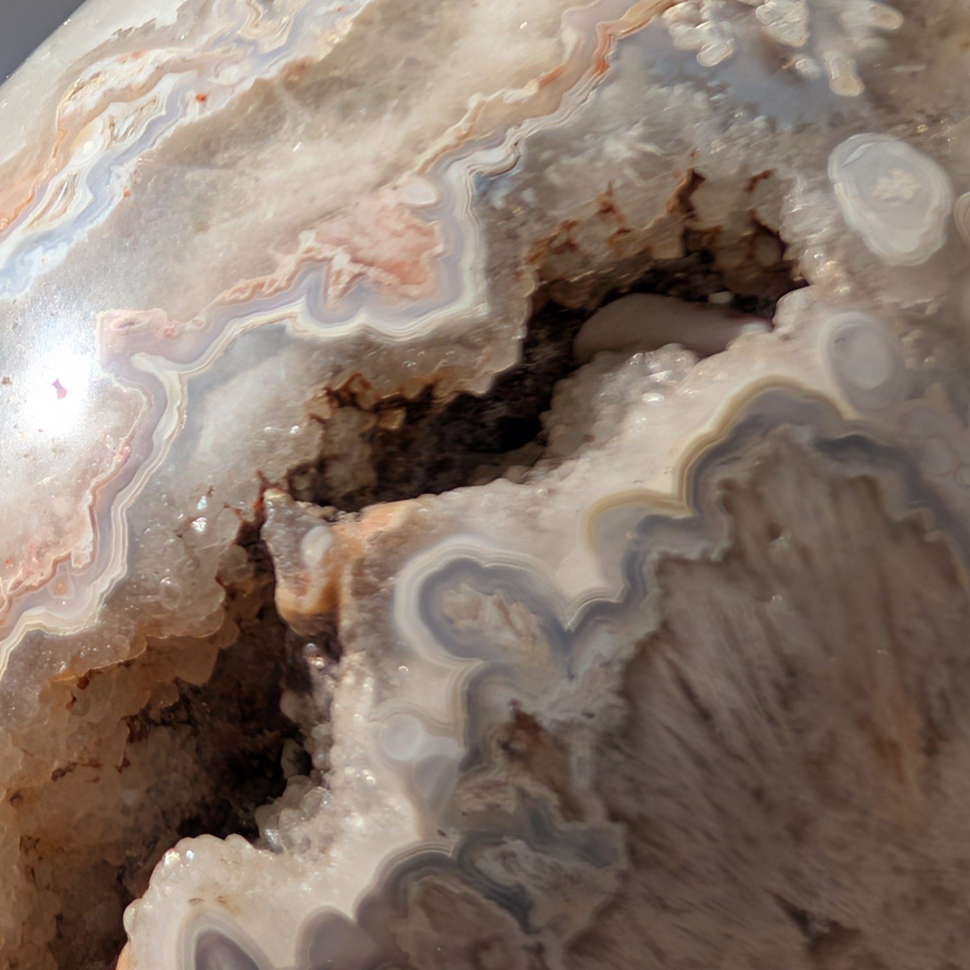 Ein monumentaler, 1292g schwerer Kristallschädel 'Der Wächter der Freude' aus Crazy Lace Achat mit hypnotischen Mustern und einer großen, offenen Druzy-Geode am Hinterkopf.