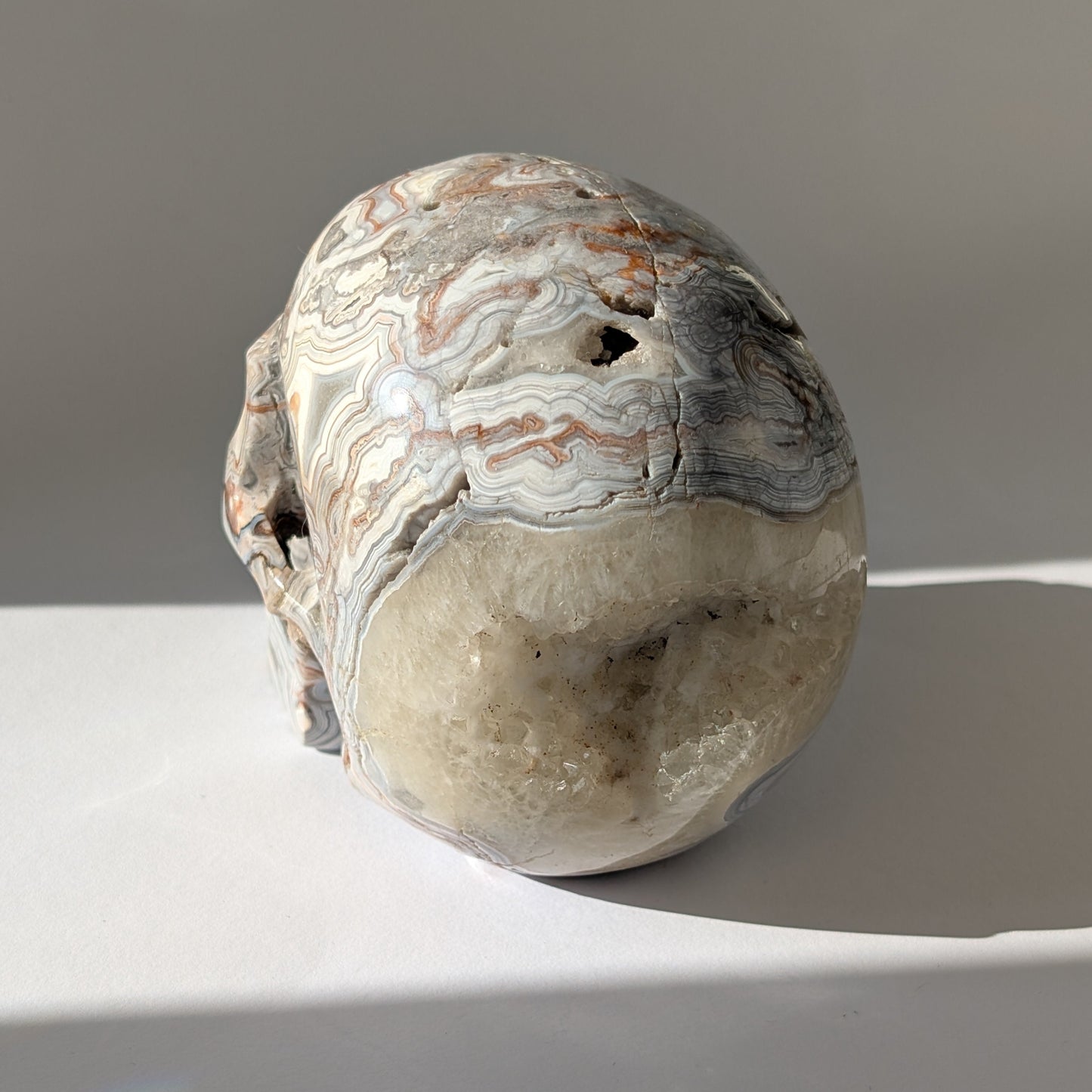 Ein monumentaler, 1301g schwerer Kristallschädel 'Rondar' aus Crazy Lace Achat mit hypnotischen Mustern und einer großen, offenen Druzy-Geode am Hinterkopf.