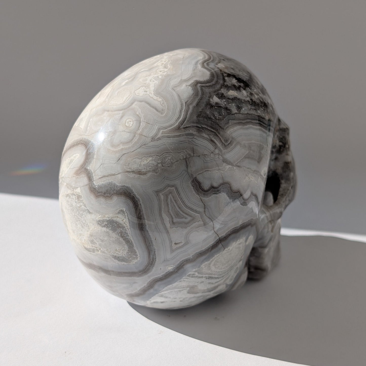 Ein monumentaler, 1352g schwerer Kristallschädel 'Lea' aus Gebändertem Achat mit hypnotischen, fließenden Bändern in Grau-, Schwarz- und Weißtönen.