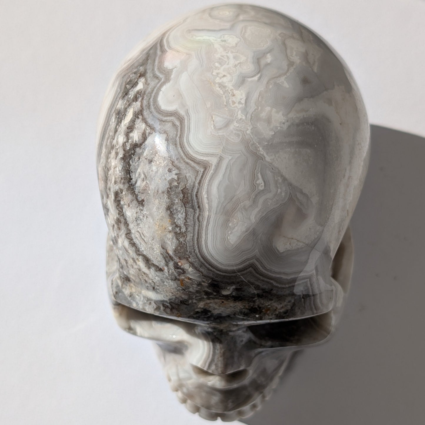 Ein monumentaler, 1352g schwerer Kristallschädel 'Lea' aus Gebändertem Achat mit hypnotischen, fließenden Bändern in Grau-, Schwarz- und Weißtönen.