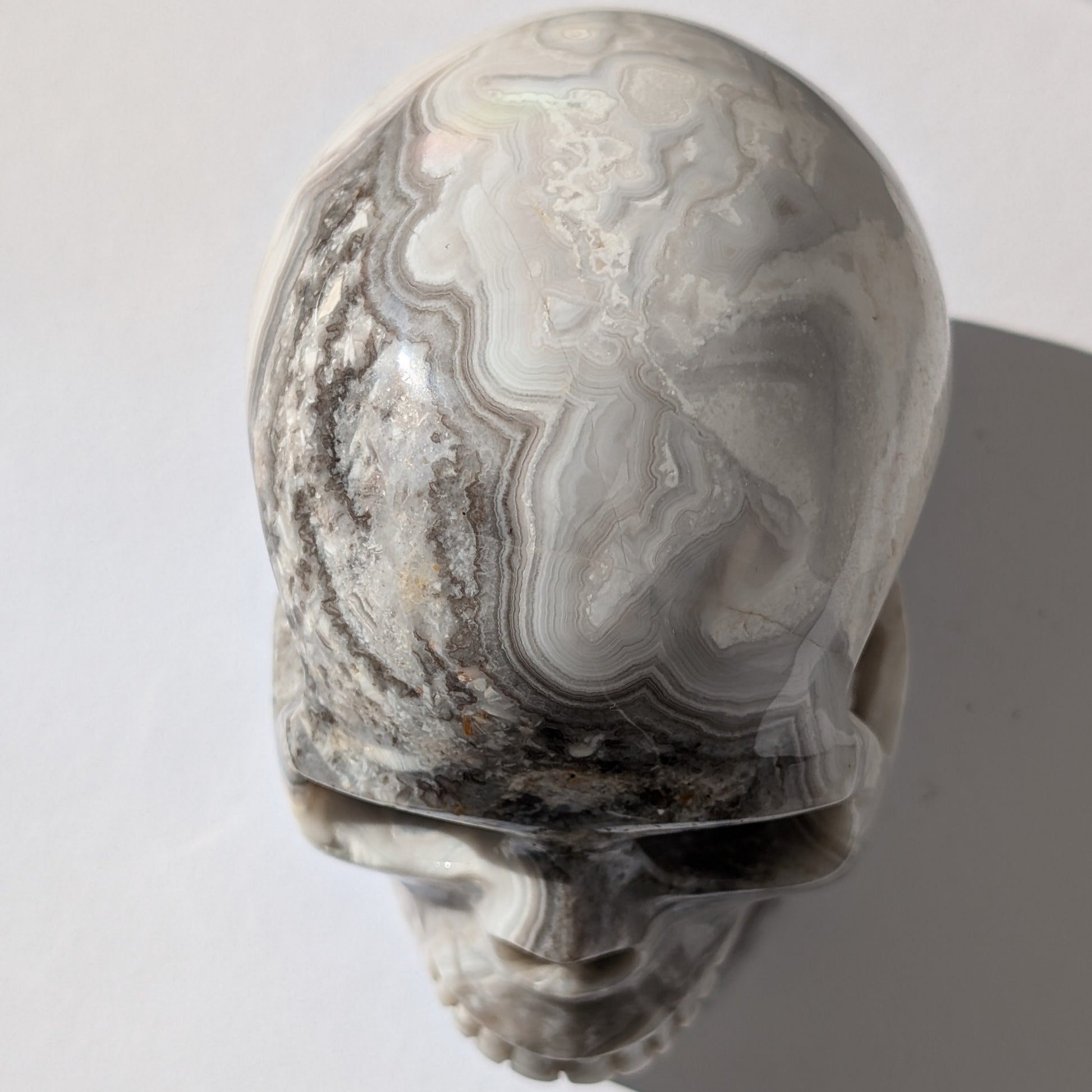 Ein monumentaler, 1352g schwerer Kristallschädel 'Lea' aus Gebändertem Achat mit hypnotischen, fließenden Bändern in Grau-, Schwarz- und Weißtönen.