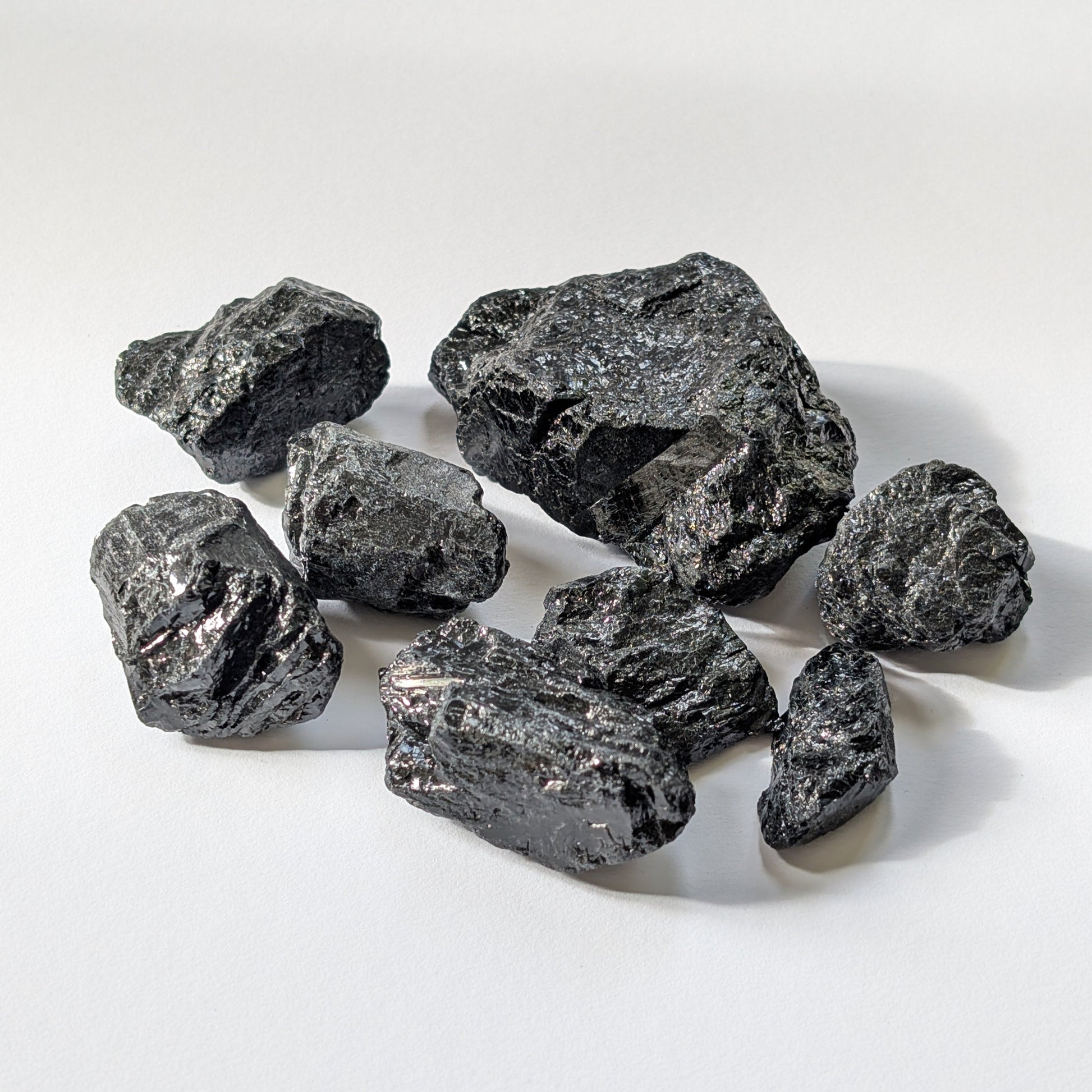 Eine Gruppe von rohen, tiefschwarzen Turmalin-Brocken (Schörl) mit glasartigem Glanz auf einer weißen Oberfläche.