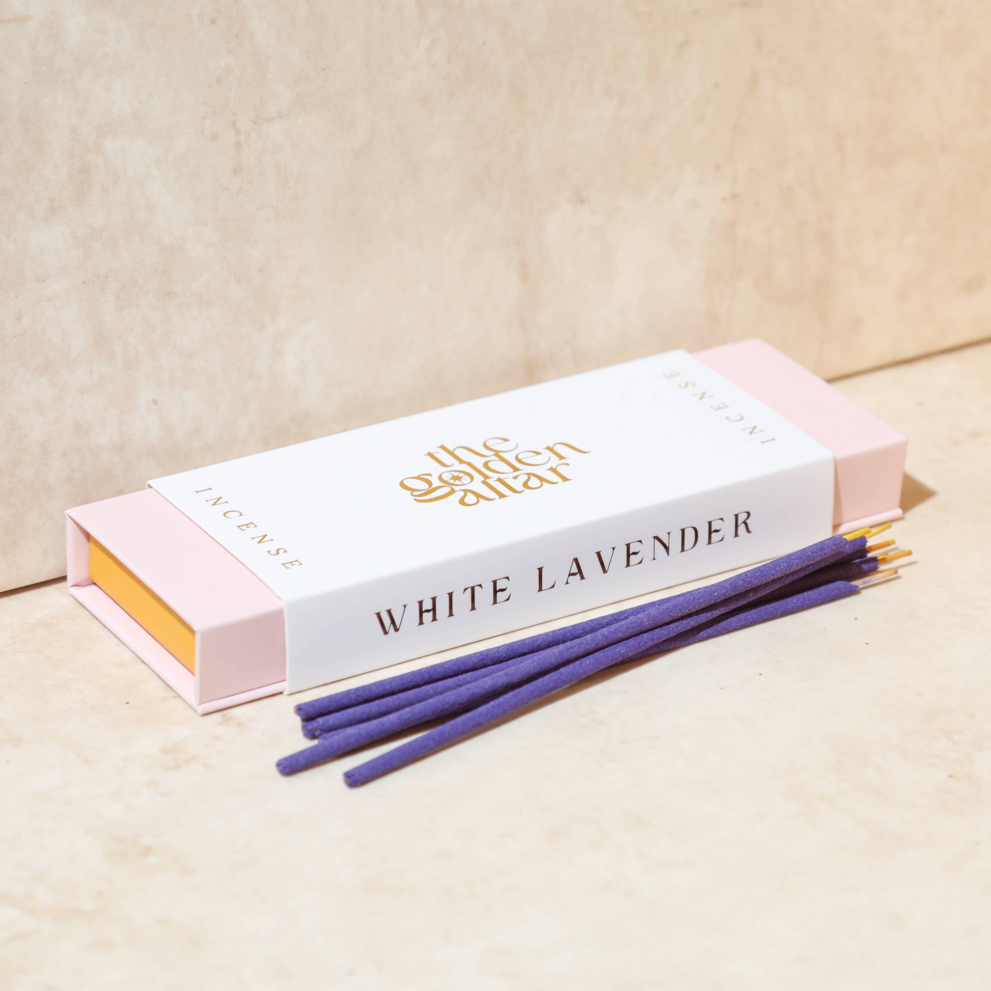 Eine cremeweiße Box von The Golden Altar mit 30 lila Weiße Lavendel Räucherstäbchen, die daneben liegen.