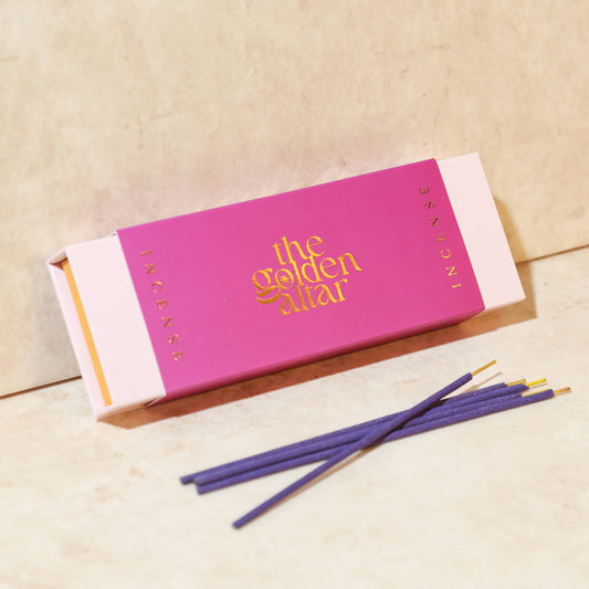Eine fuchsiafarbene Box von The Golden Altar mit 30 dunklen Jasmin Räucherstäbchen, die daneben liegen.