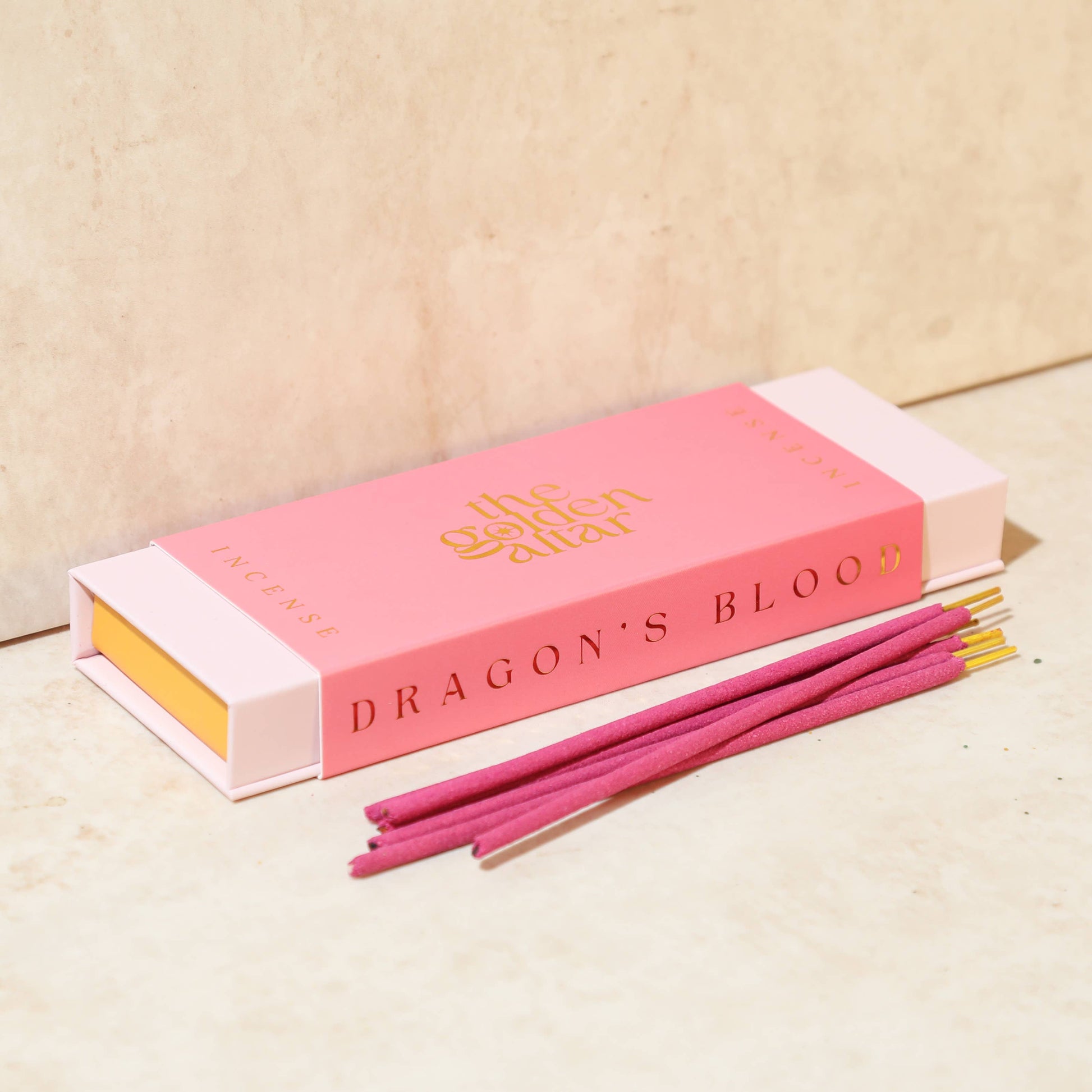 Eine leuchtend pinke Box von The Golden Altar mit 30 roten Drachenblut Räucherstäbchen, die daneben liegen.