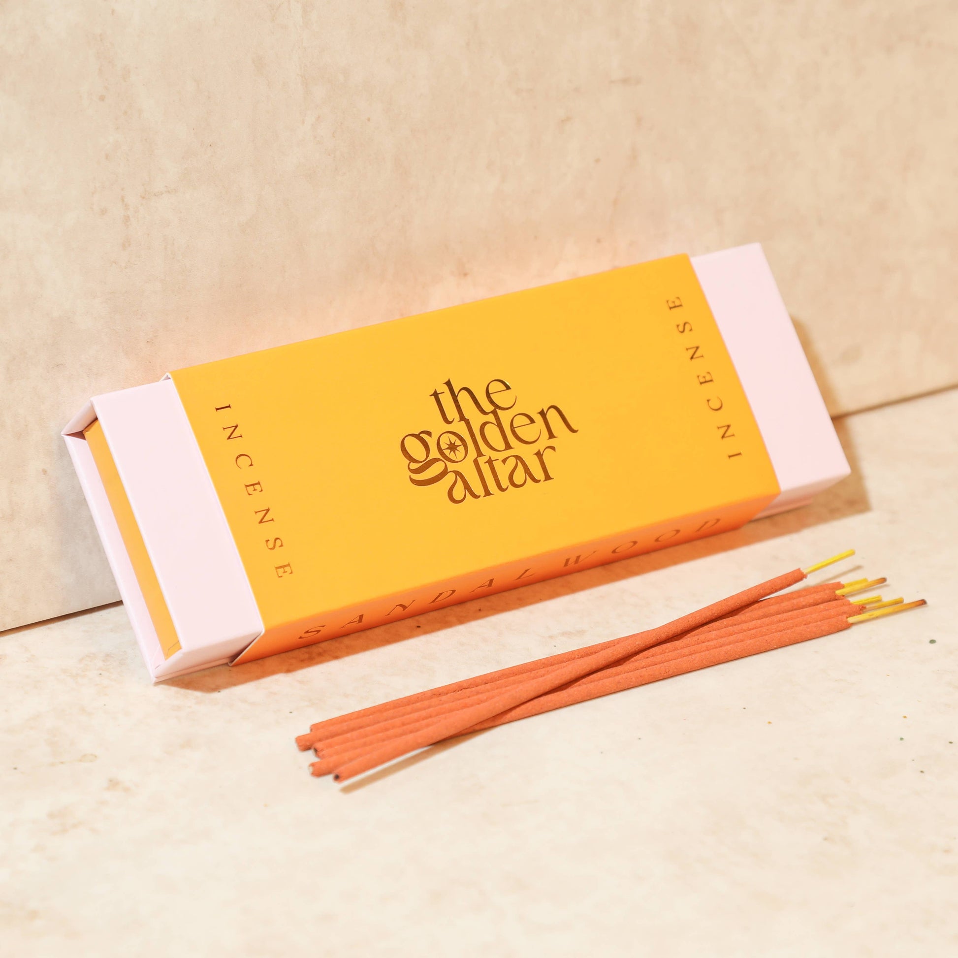 Eine orangefarbene Box von The Golden Altar mit 30 Sandelholz Räucherstäbchen, die daneben liegen.