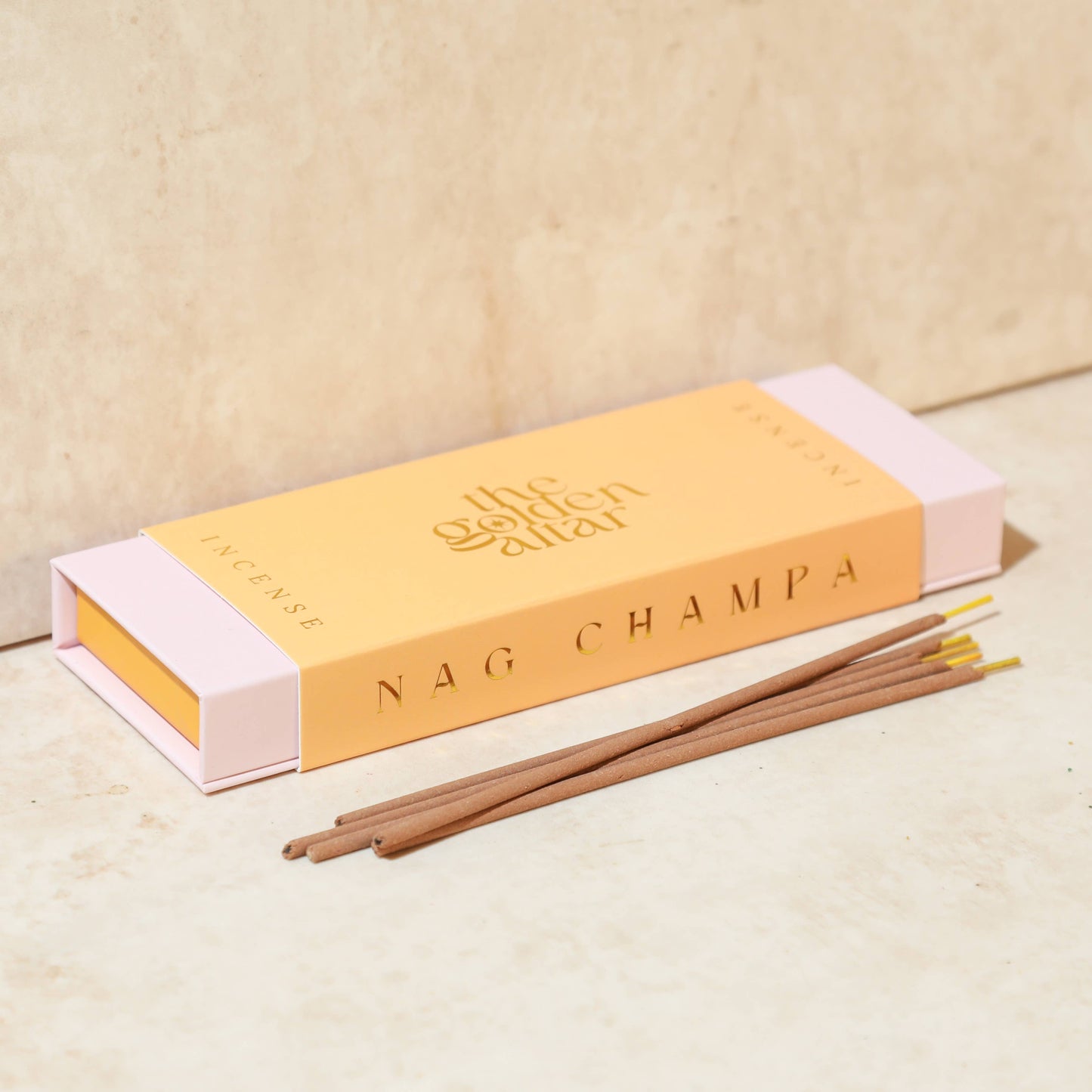 Eine pfirsichfarbene Box von The Golden Altar mit 30 Nag Champa Räucherstäbchen, die daneben liegen.