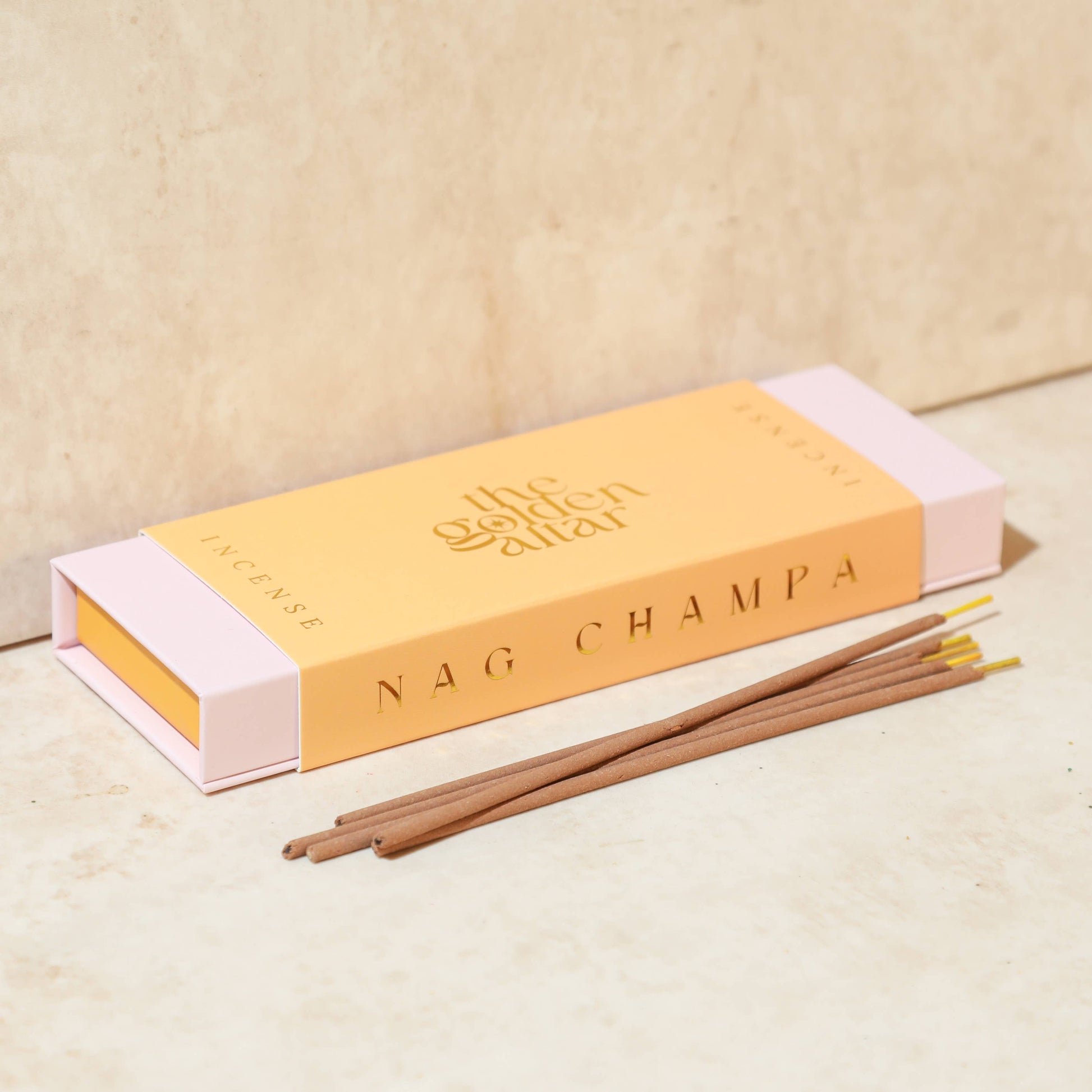 Eine pfirsichfarbene Box von The Golden Altar mit 30 Nag Champa Räucherstäbchen, die daneben liegen.