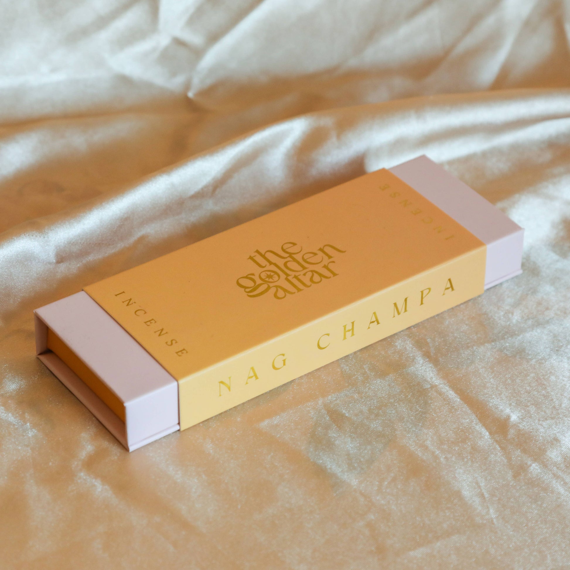 Eine pfirsichfarbene Box von The Golden Altar mit 30 Nag Champa Räucherstäbchen, die daneben liegen.