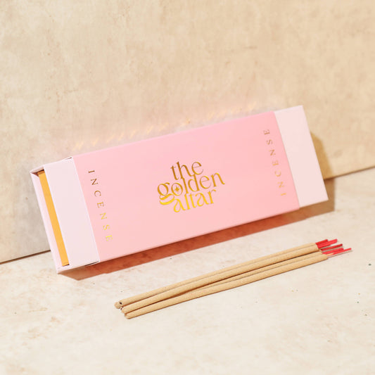 Eine rosa-orangefarbene Box von The Golden Altar mit 30 Rose & Vetiver Räucherstäbchen, die daneben liegen.