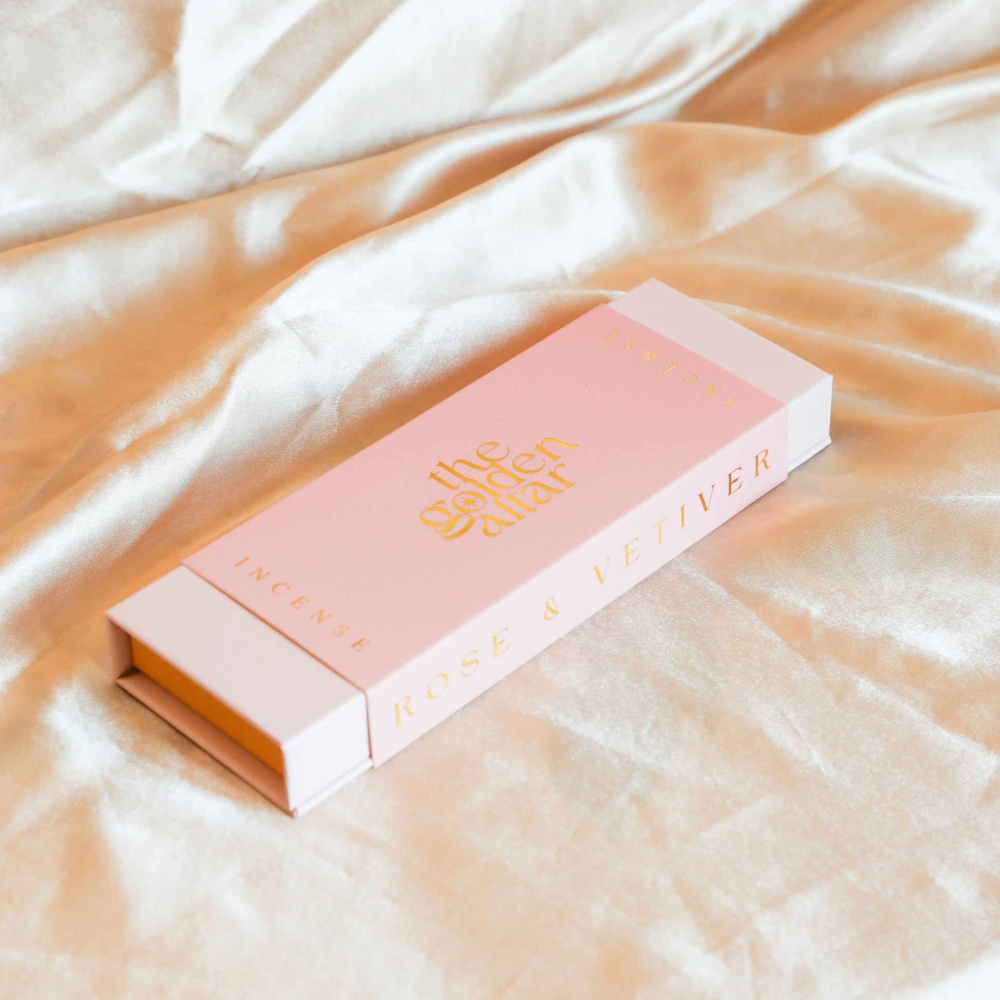 Eine rosa-orangefarbene Box von The Golden Altar mit 30 Rose & Vetiver Räucherstäbchen, die daneben liegen.