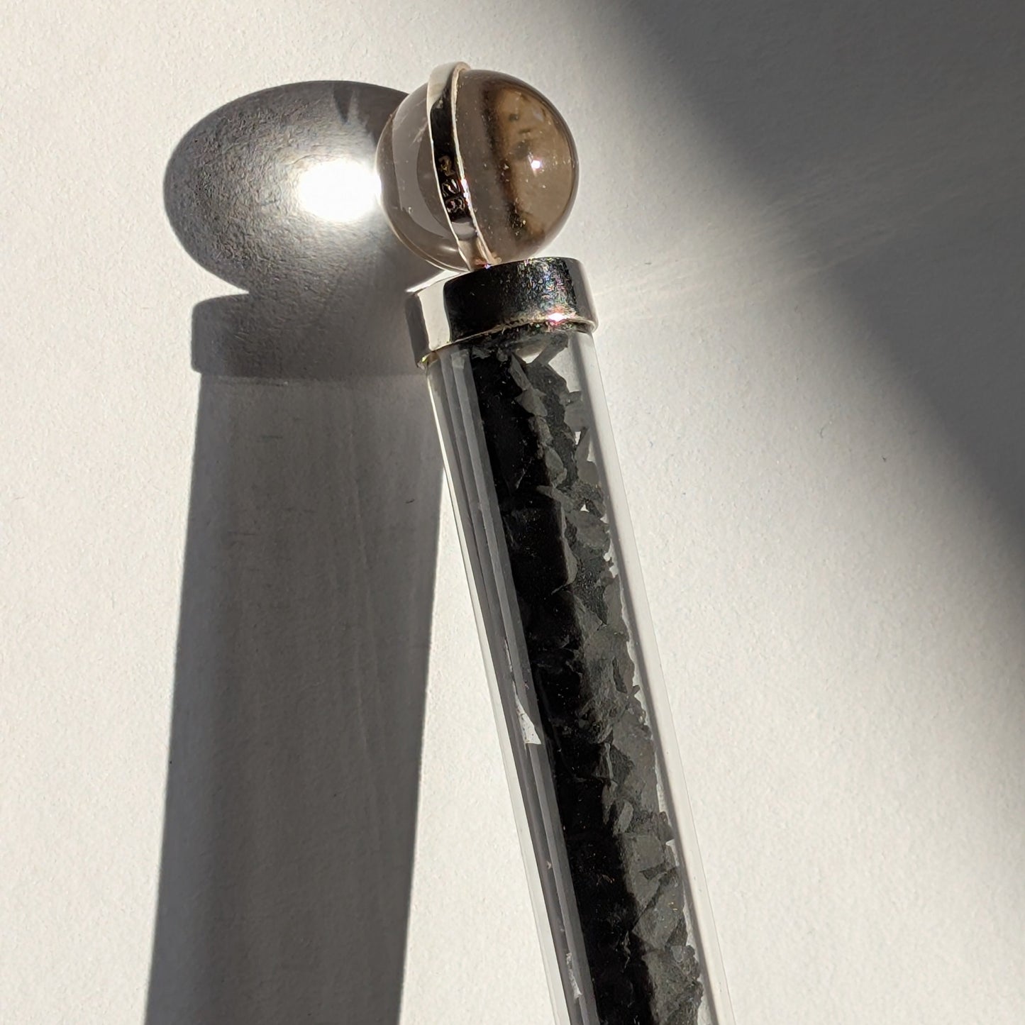 Eleganter Generatorstab mit Schungit-Füllung, Quarzkugel und schwarzer Spitze in hellem Licht.