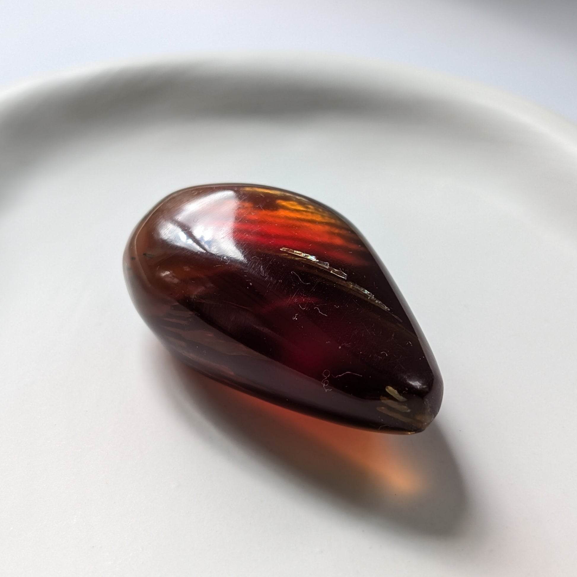 Eleganter, tropfenförmiger Bicolor-Bernstein 'Die Träne der Sonne', der von tiefem Kirschrot zu leuchtendem Gold schimmert.