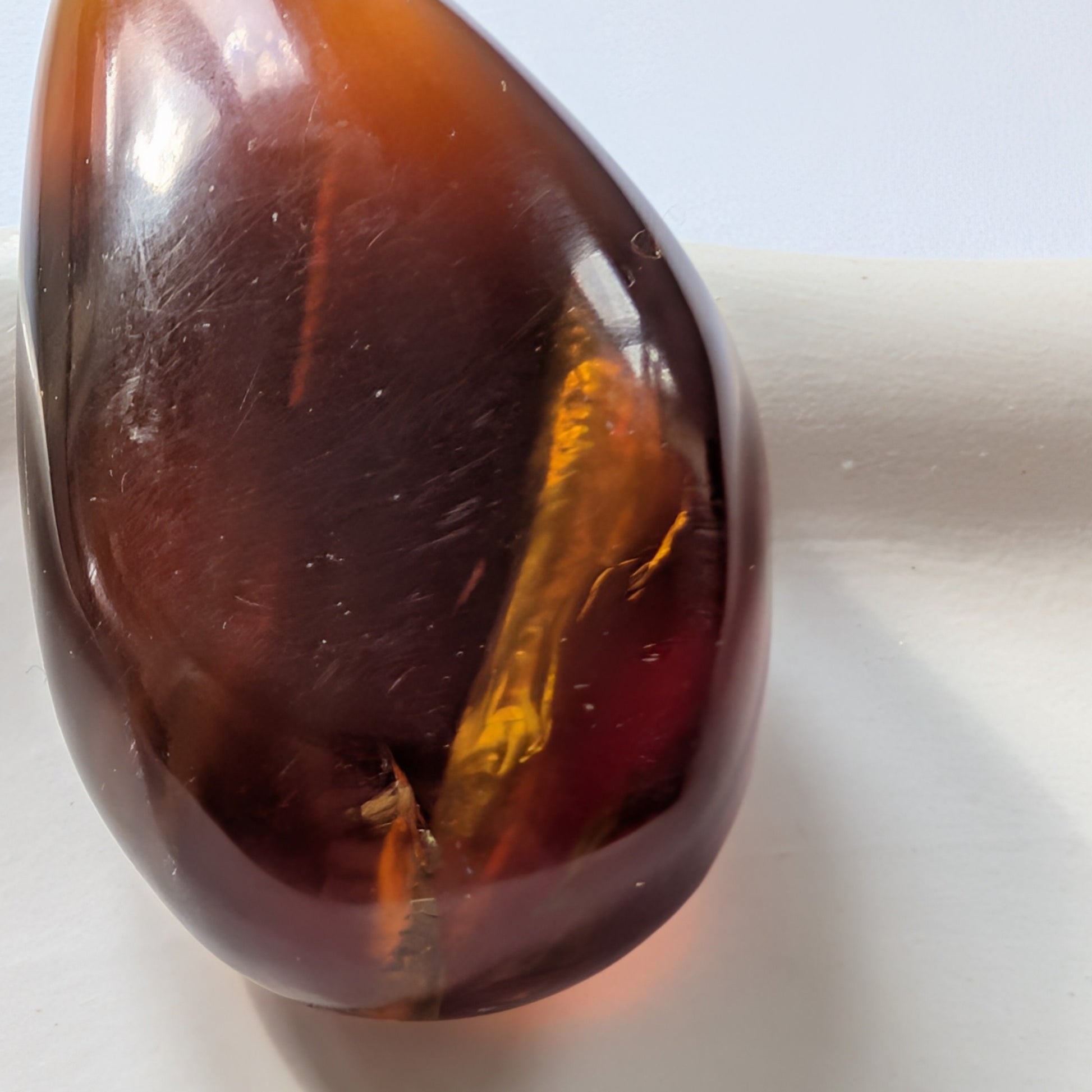 Eleganter, tropfenförmiger Bicolor-Bernstein 'Die Träne der Sonne', der von tiefem Kirschrot zu leuchtendem Gold schimmert.