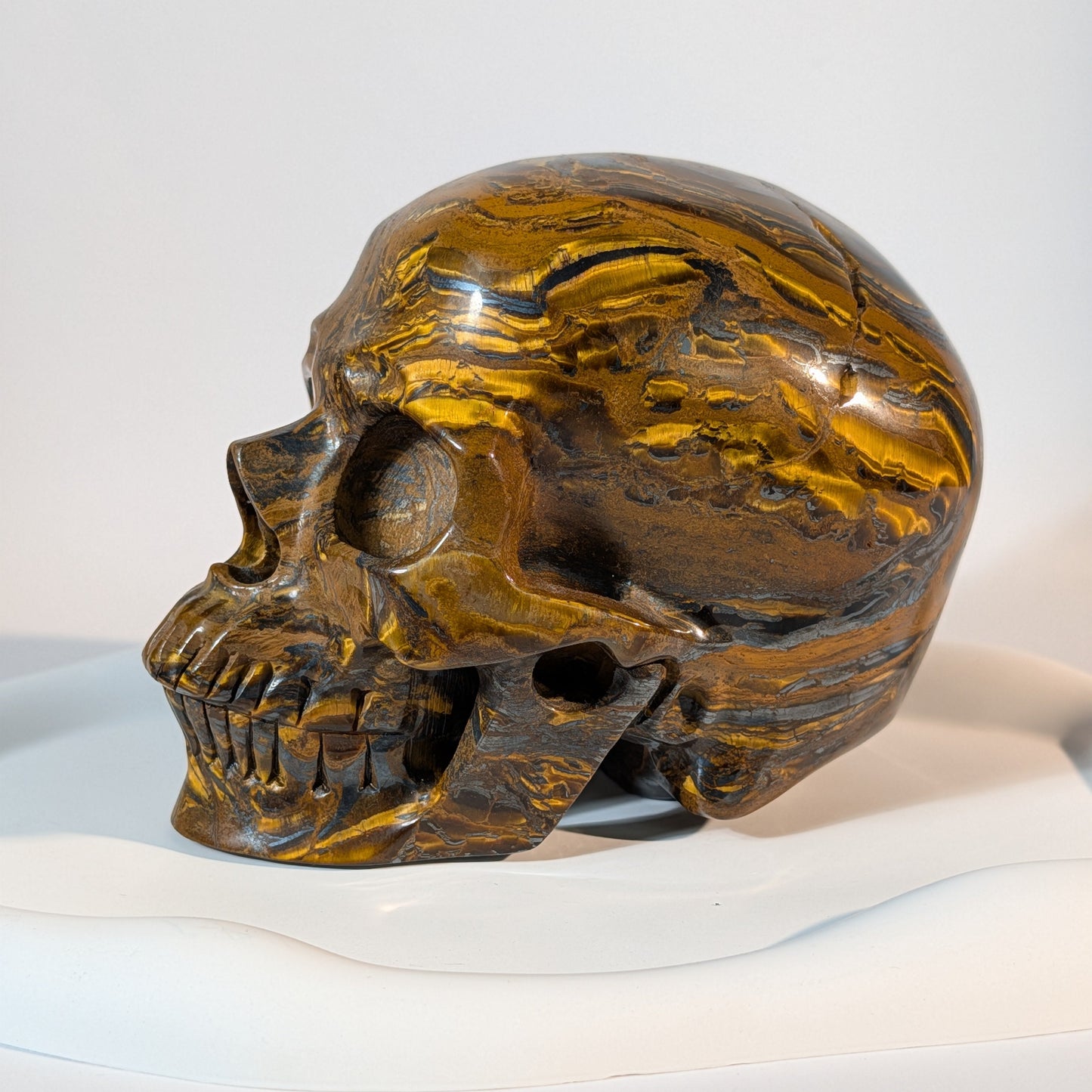 Gigantischer Kristallschädel, gezeichnet von markanten, zweifarbigen Bändern aus goldenem Tigerauge und silbrig-metallischem Hämatit.