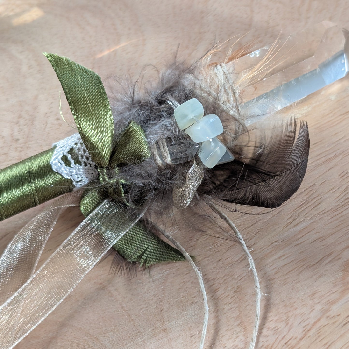 Handgefertigter Zauberstab mit einem goldgelben Citrin und schimmerndem Drusenquarz, verziert mit Federn und einem grünen Band, auf einer Holzplatte.