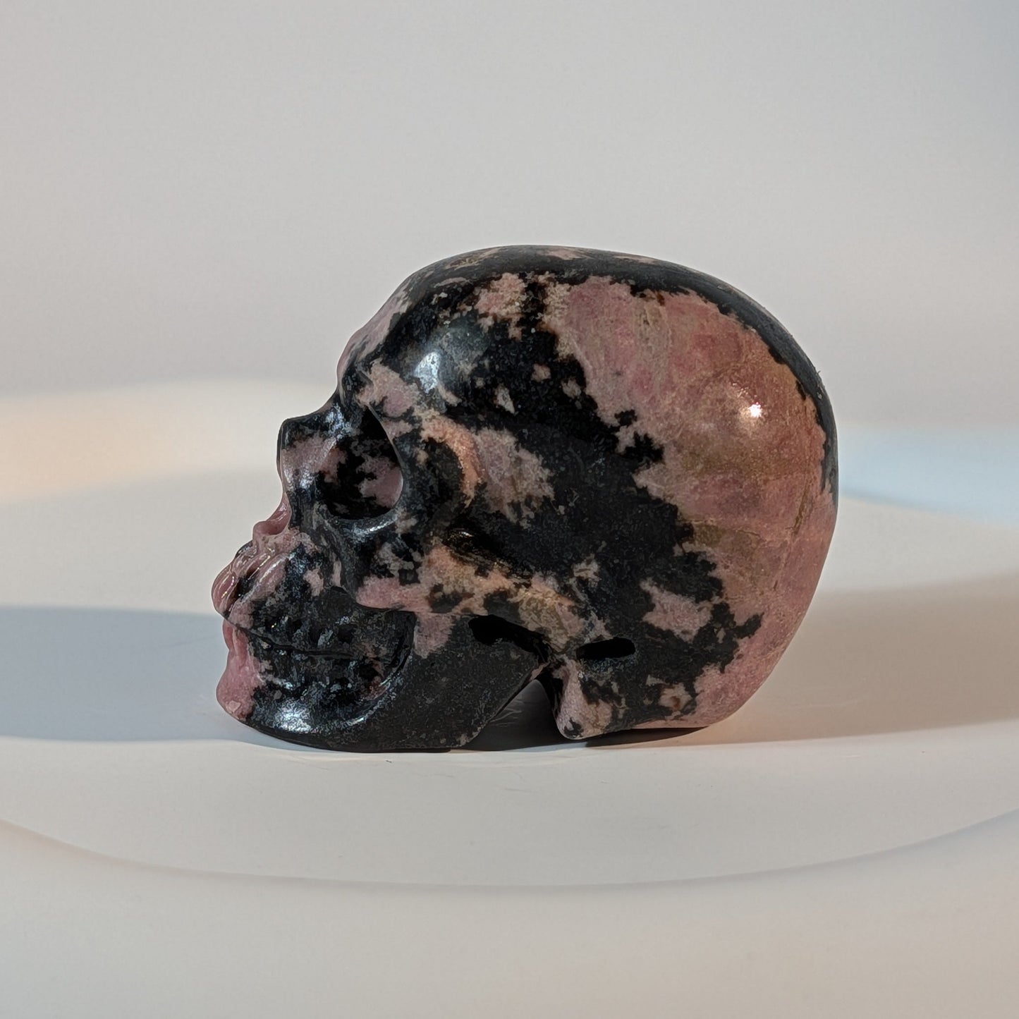Handgeschnitzter Kristallschädel Sariel aus echtem Rhodonit, 114 Gramm schwer, mit markanter rosa-schwarzer Maserung für emotionale Heilung und Erdung.