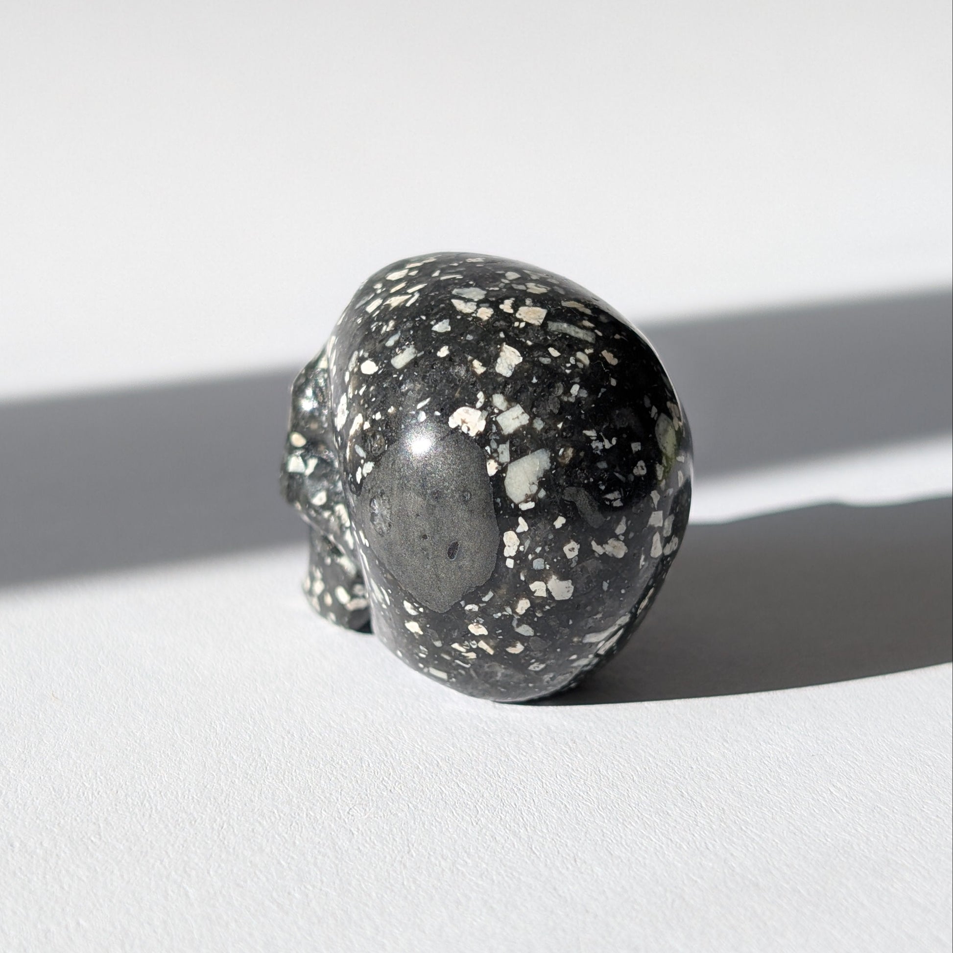 Kleiner Kristallschädel "Blyss" (87g) aus dunkelgrauem Gabbro (Mystic Merlinite) mit hellen Sprenkeln.