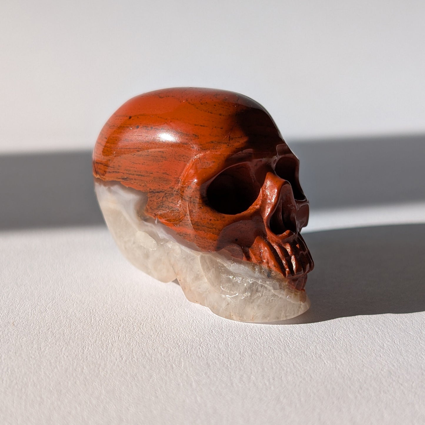 Kleiner Kristallschädel "Edun" (86g), halb aus rotem Jaspis, halb aus hellem Quarz.
