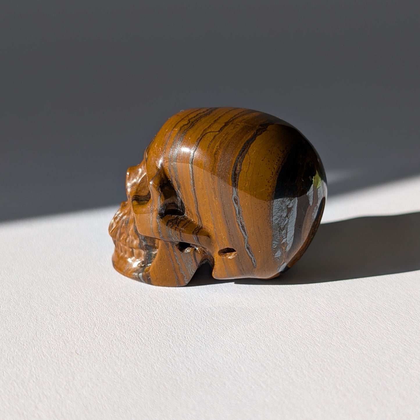 Kleiner Kristallschädel "Rogras" (104g) aus gebändertem Tigereisen mit goldener Chatoyancy.