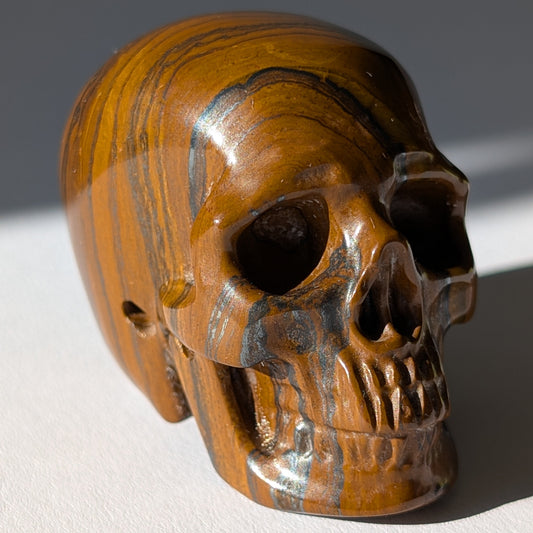 Kleiner Kristallschädel "Rogras" (104g) aus gebändertem Tigereisen mit goldener Chatoyancy.