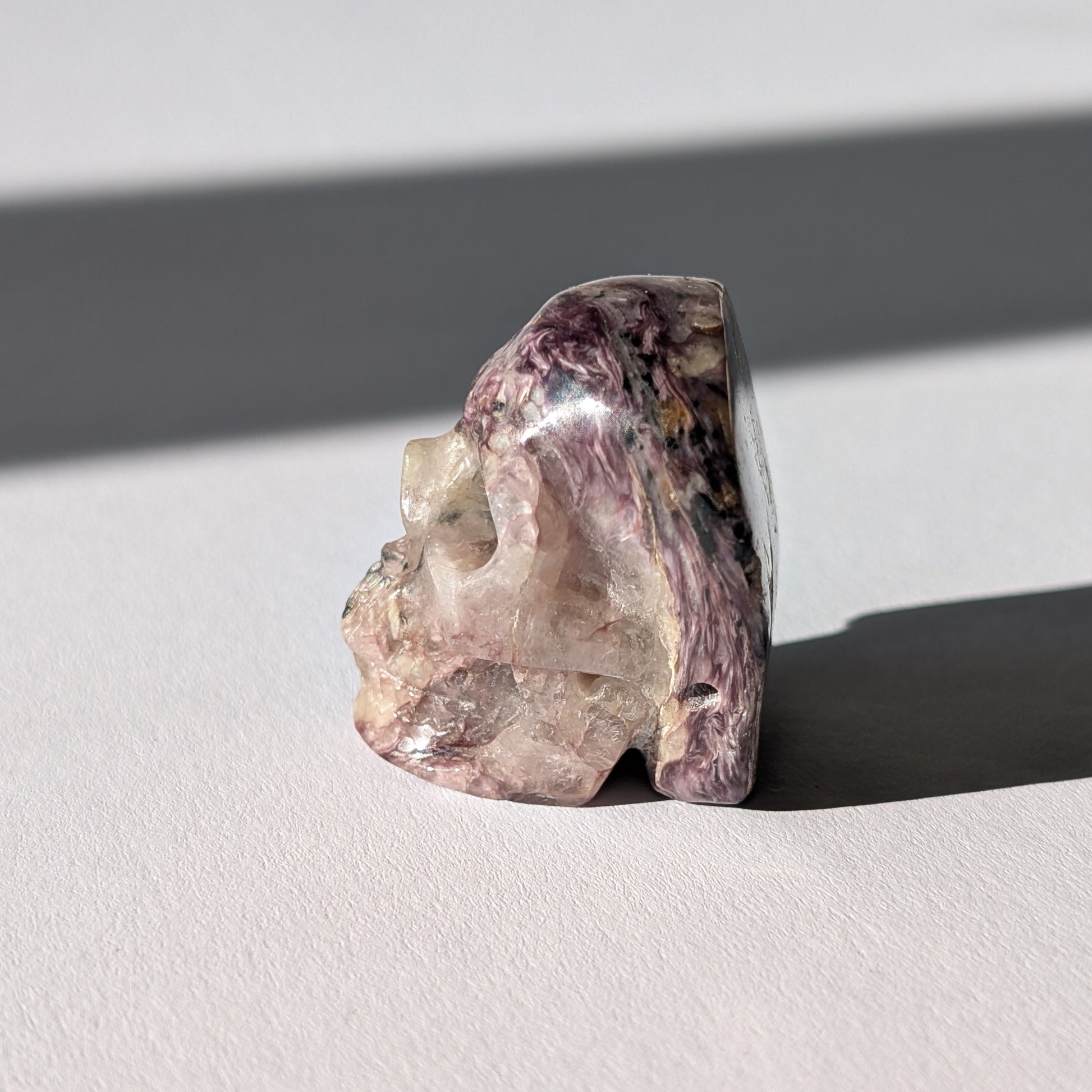 Kleiner Kristallschädel "Veykor" (51g) aus violettem Charoit mit seidigen Wirbeln.