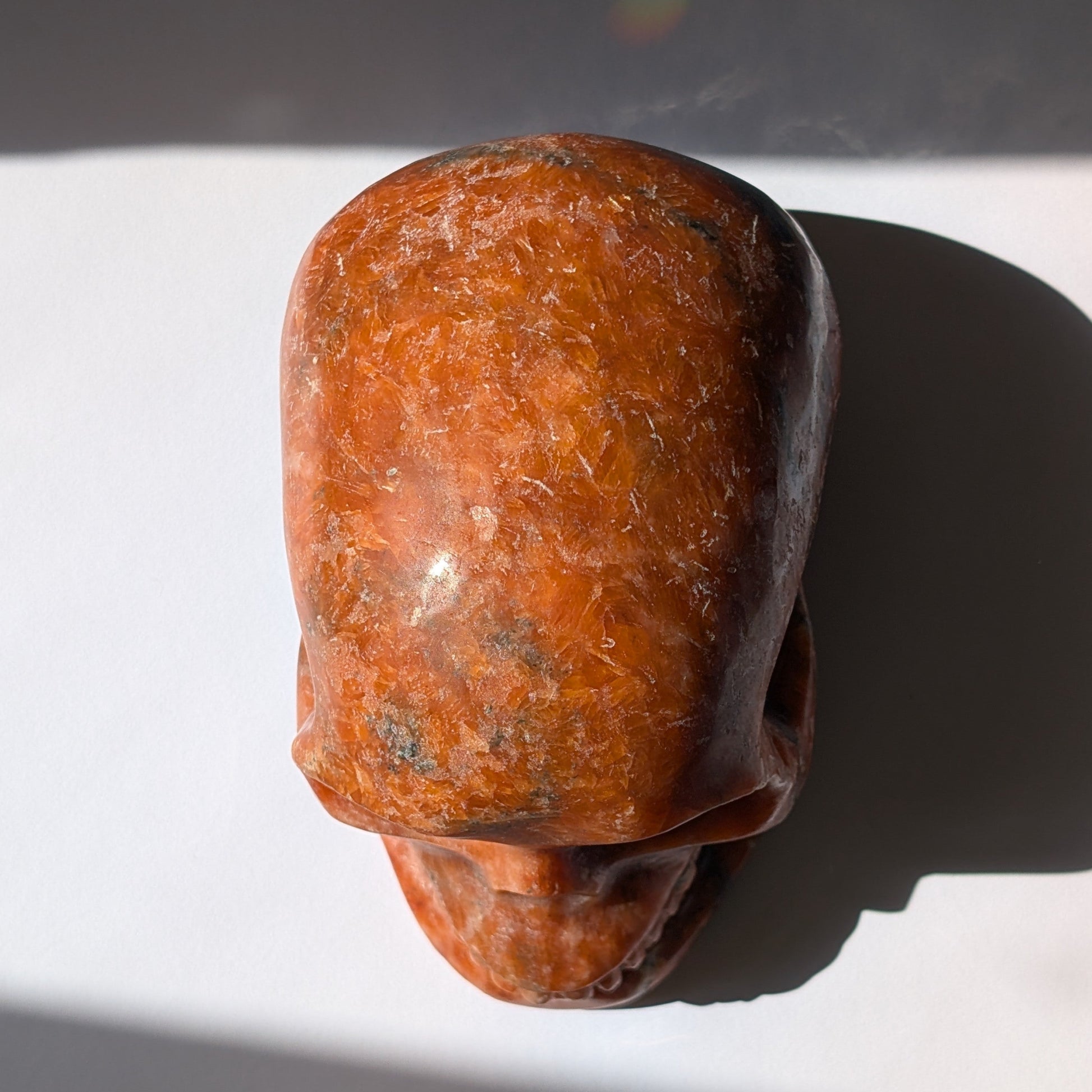 Kristallschädel "Aurelius" aus sonnenorangem Sonnenstein mit dunklen Einschlüssen.