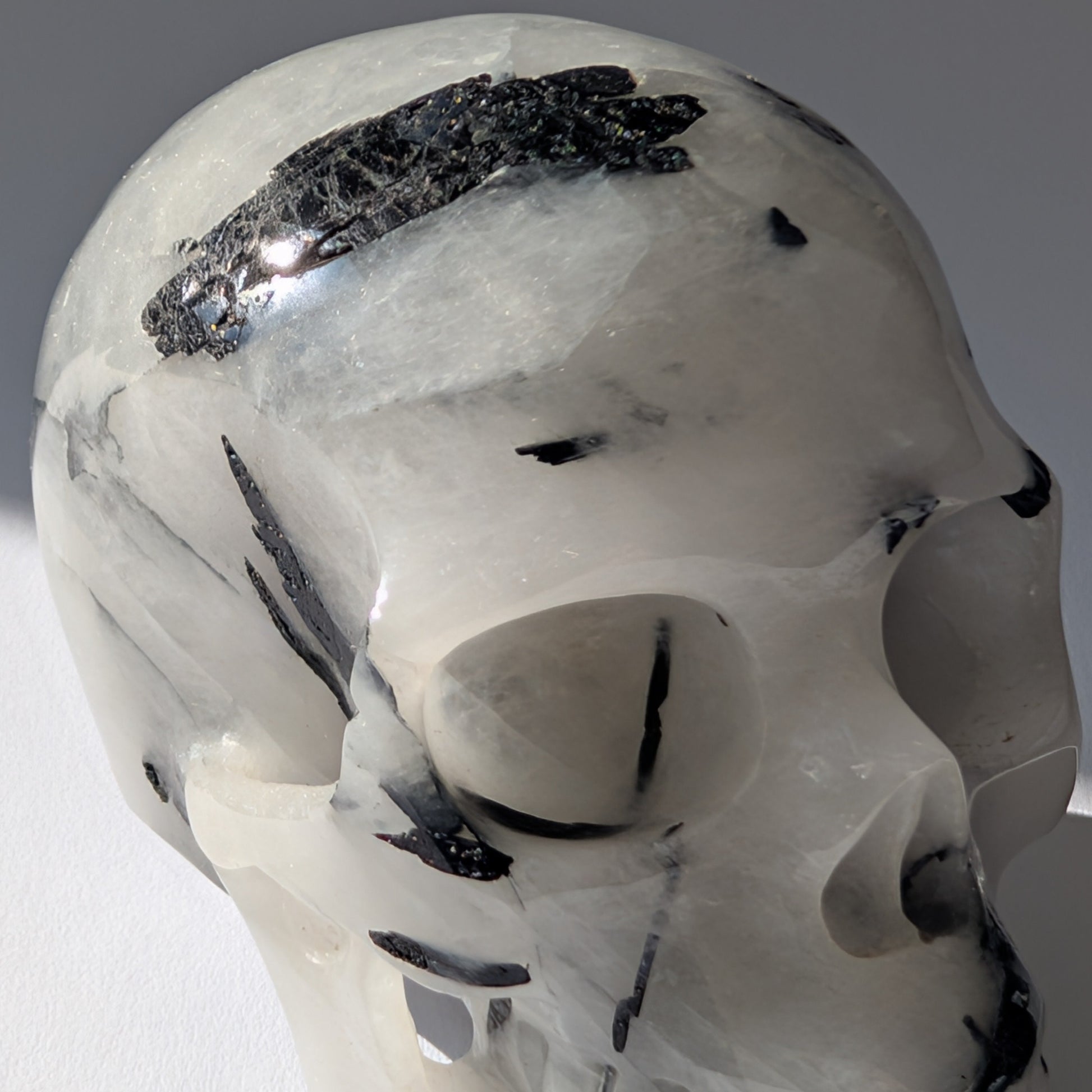 Kristallschädel "Hokan" (436g) aus klarem Quarz mit schwarzen Turmalin-Nadeln.