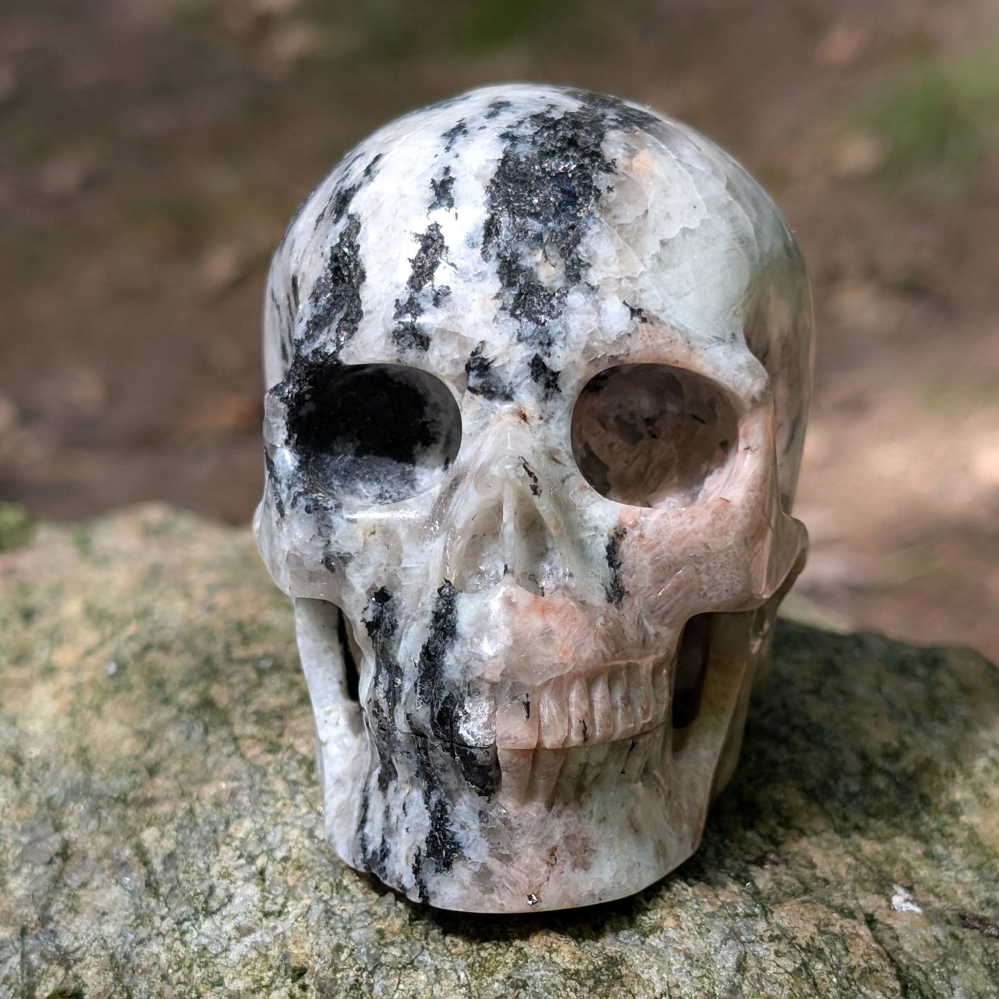 Kristallschädel "Sternenstaub" aus Granit mit schwarzer, weißer und rosafarbener Maserung.