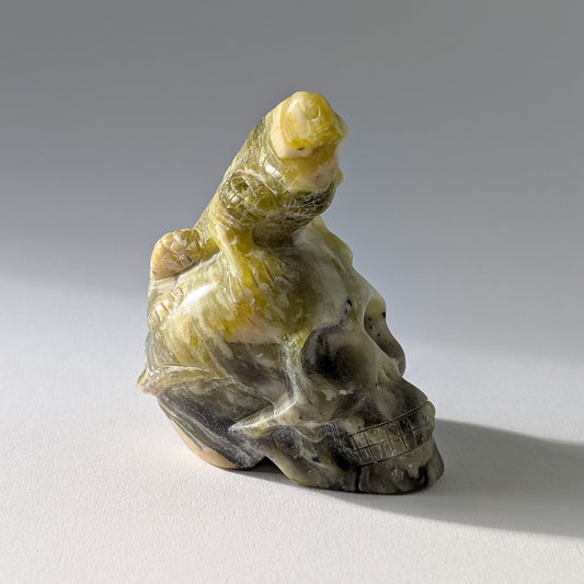 Kristallschädel "Theuth" (140g) aus Serpentin mit einer geschnitzten Eidechse auf dem Kopf.
