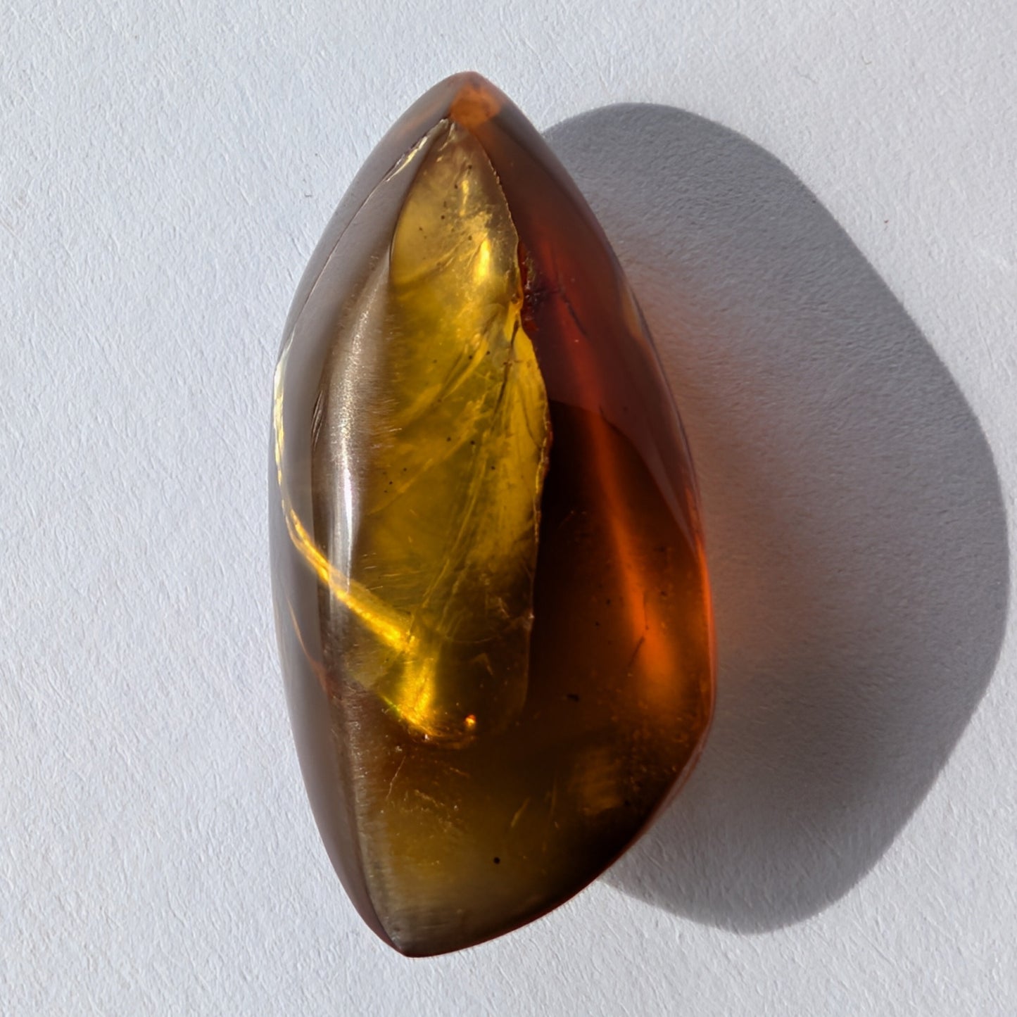 Kunstvoll geschliffener Bicolor-Bernstein 'Die Flamme der Vorzeit' in eleganter Flammenform, der von tiefrot zu gold leuchtet.