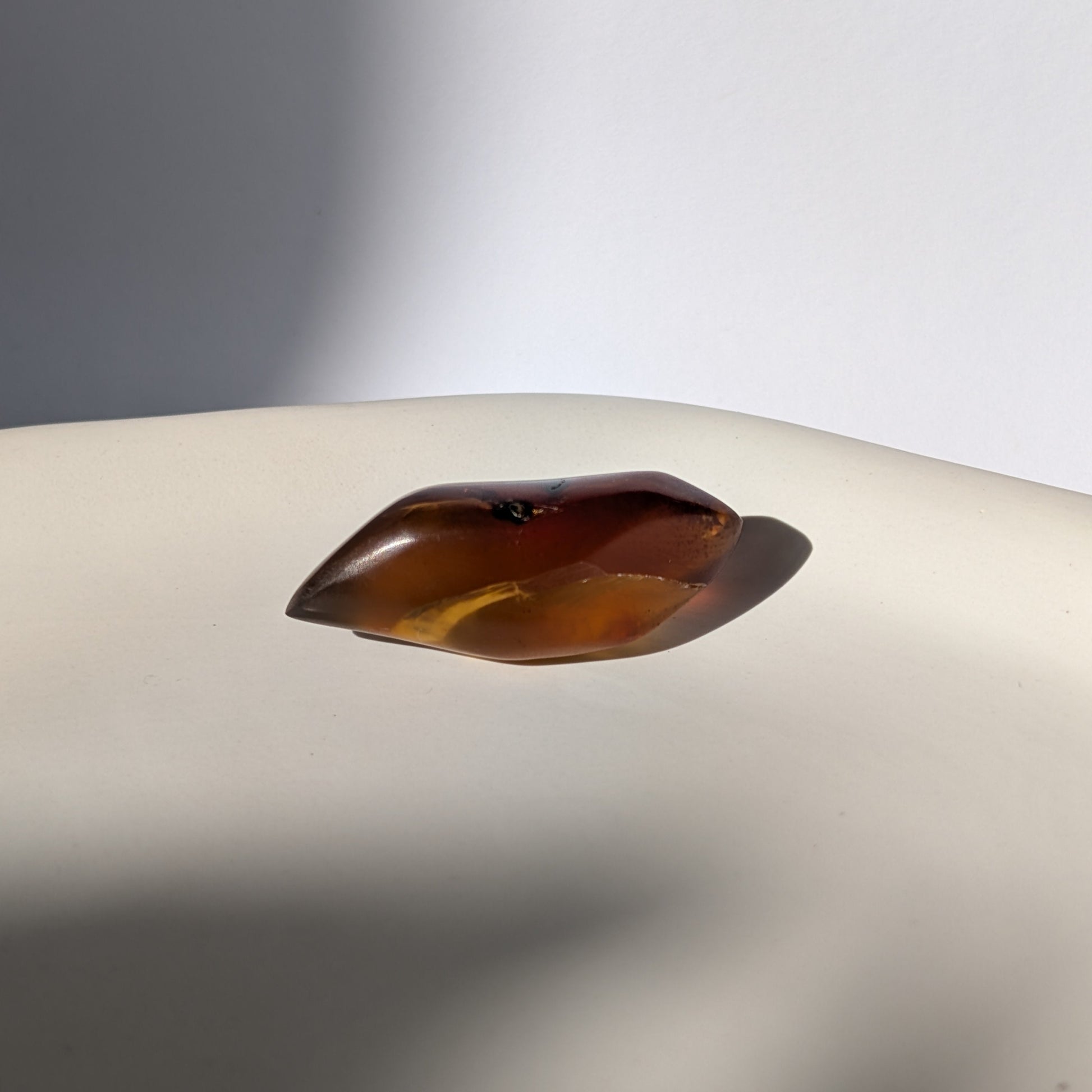 Kunstvoll geschliffener Bicolor-Bernstein 'Die Flamme der Vorzeit' in eleganter Flammenform, der von tiefrot zu gold leuchtet.