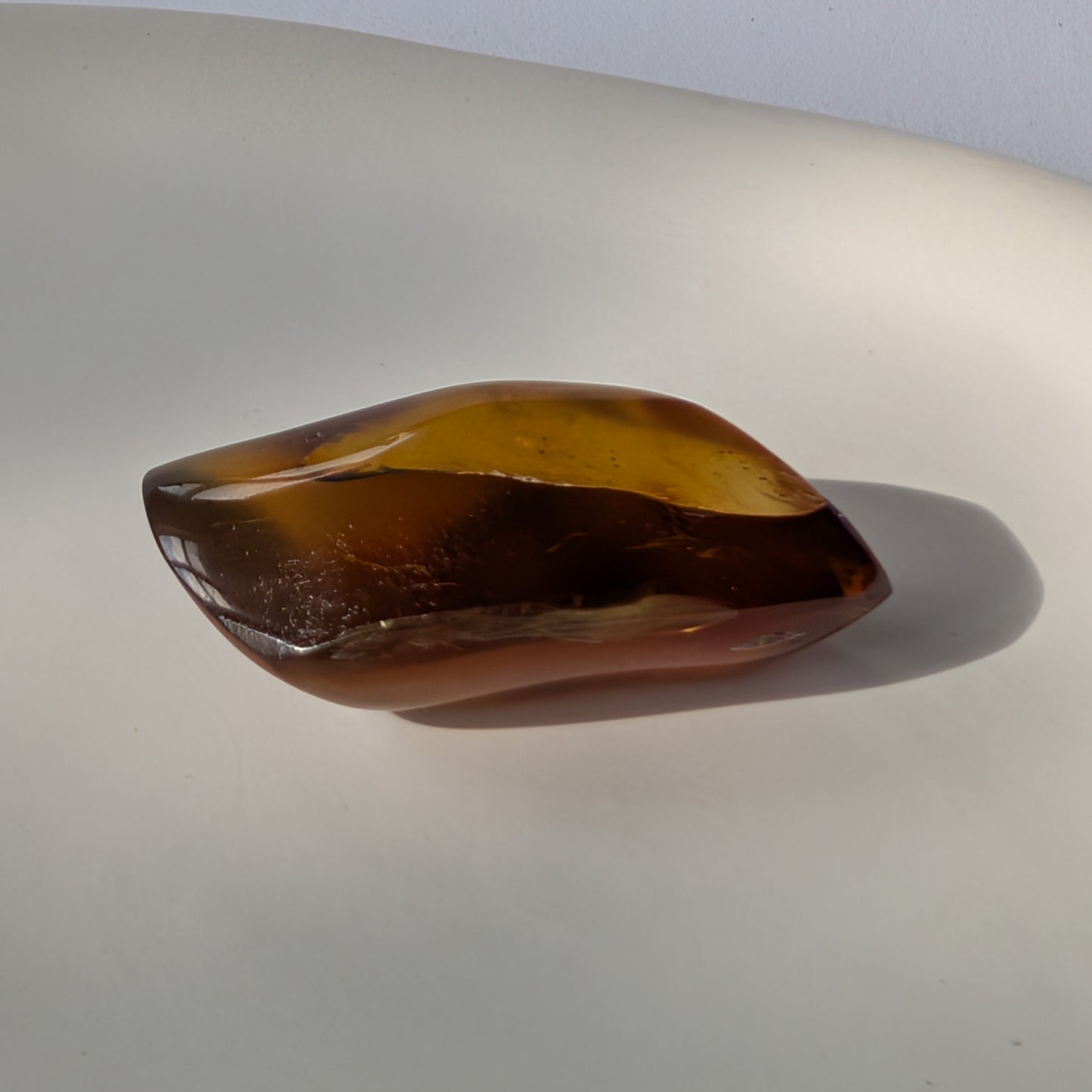 Kunstvoll geschliffener Bicolor-Bernstein 'Die Flamme der Vorzeit' in eleganter Flammenform, der von tiefrot zu gold leuchtet.