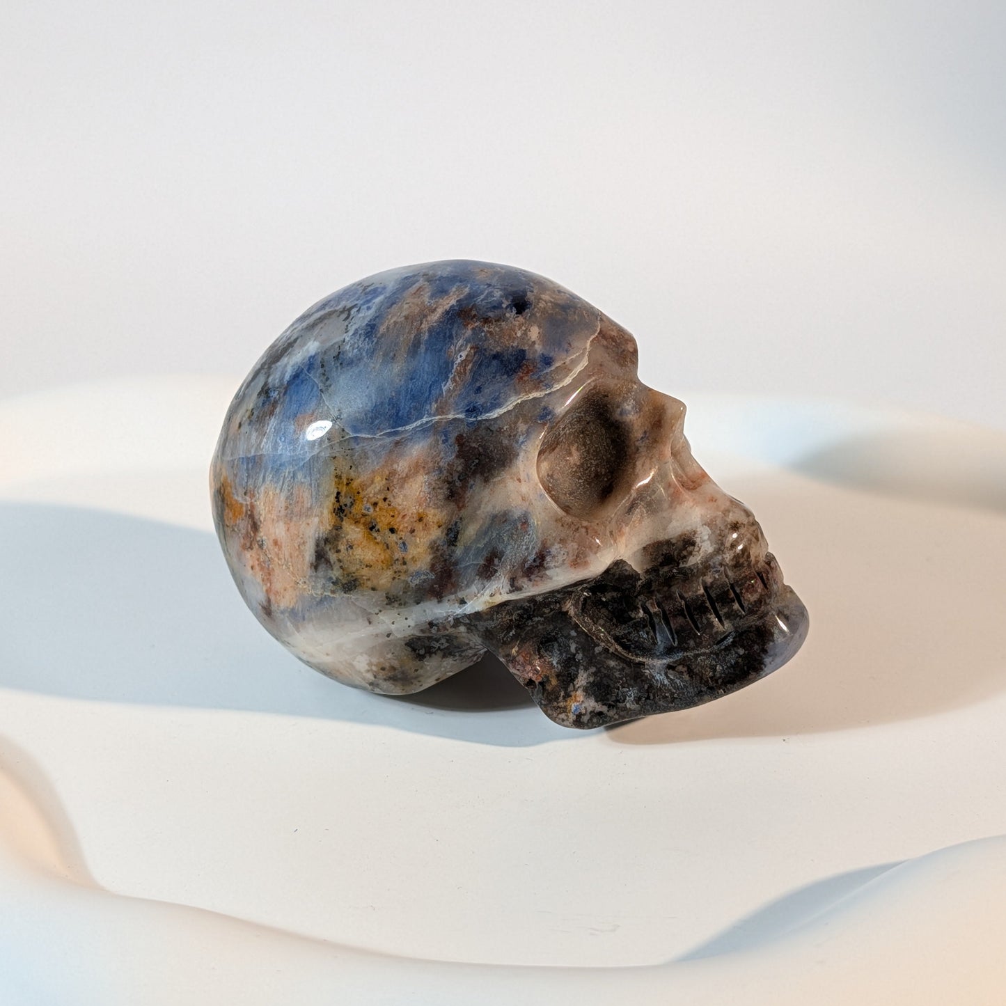 Massiver Kristallschädel Brok aus Sodalith mit zerrissener, tiefblauer, aschgrauer und rostig oranger Gesteinsmatrix.