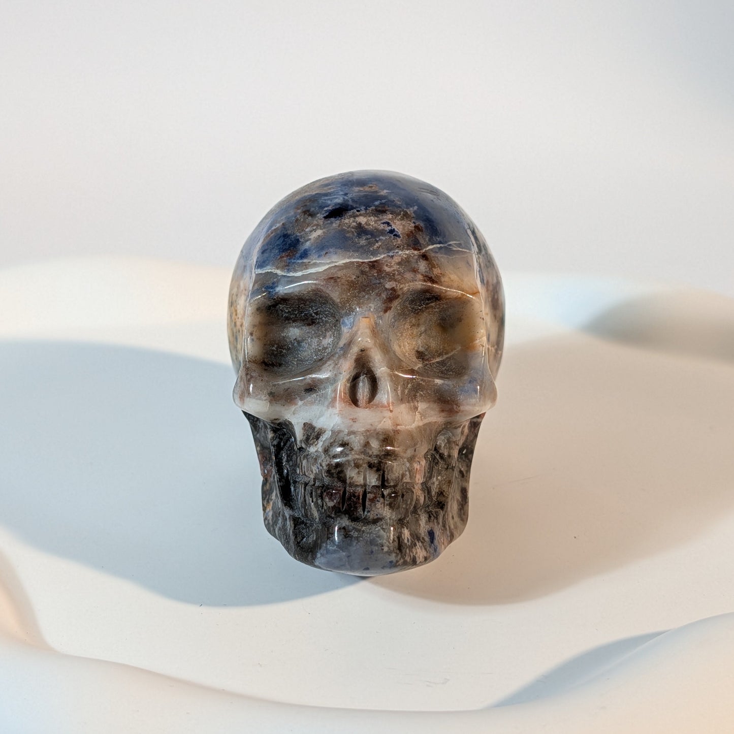 Massiver Kristallschädel Brok aus Sodalith mit zerrissener, tiefblauer, aschgrauer und rostig oranger Gesteinsmatrix.