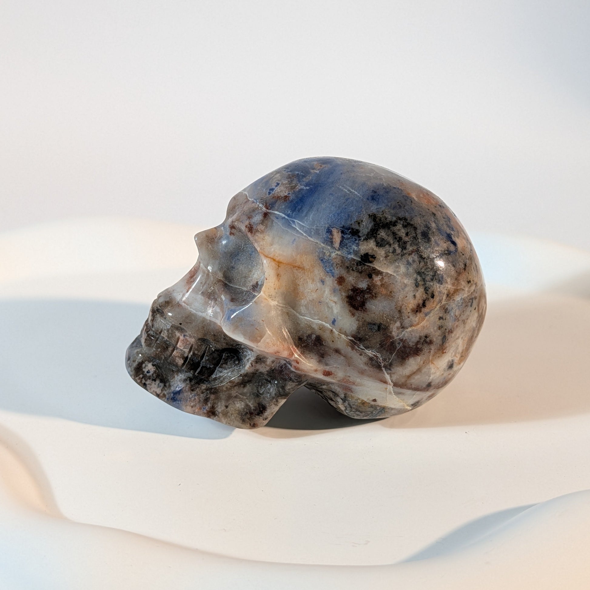 Massiver Kristallschädel Brok aus Sodalith mit zerrissener, tiefblauer, aschgrauer und rostig oranger Gesteinsmatrix.