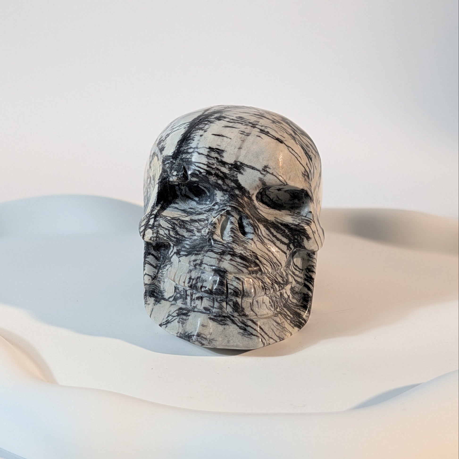 Massiver Kristallschädel Kyra aus knochenweißem Magnesit, zerschnitten von extrem harten, pechschwarzen Gesteinsadern.