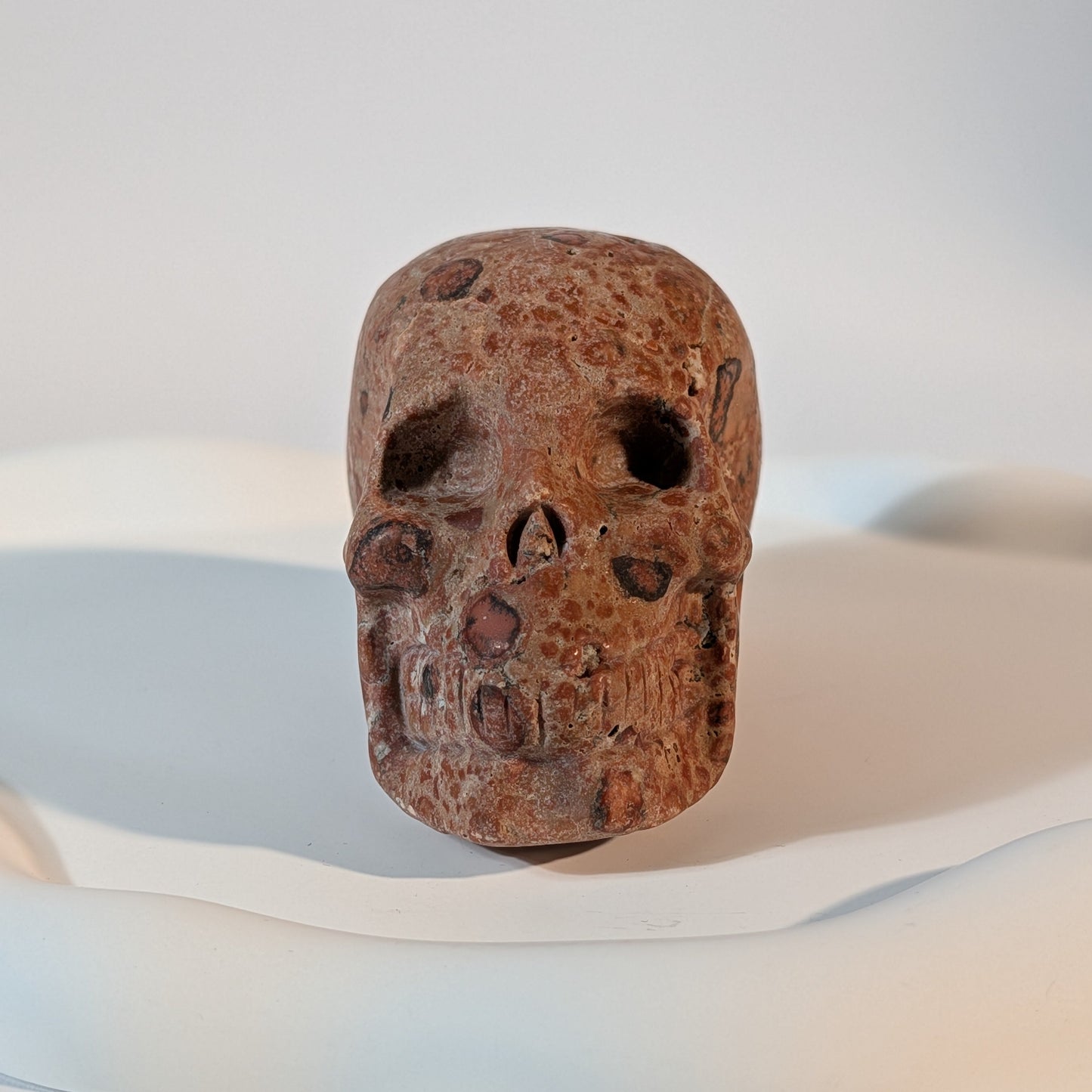 Massiver Kristallschädel Sidahan aus Rhyolith mit blutroter und rostbrauner, von Kratern und dunklen Pocken durchzogener Gesteinsmatrix.