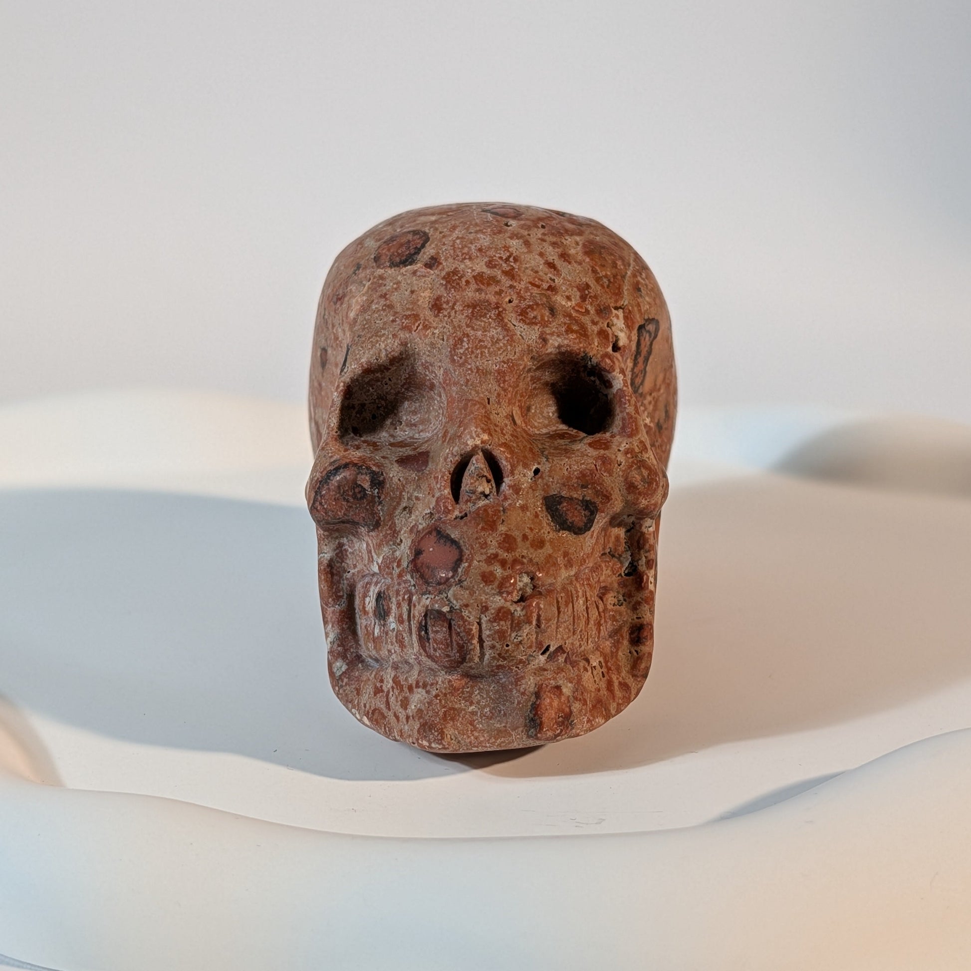 Massiver Kristallschädel Sidahan aus Rhyolith mit blutroter und rostbrauner, von Kratern und dunklen Pocken durchzogener Gesteinsmatrix.