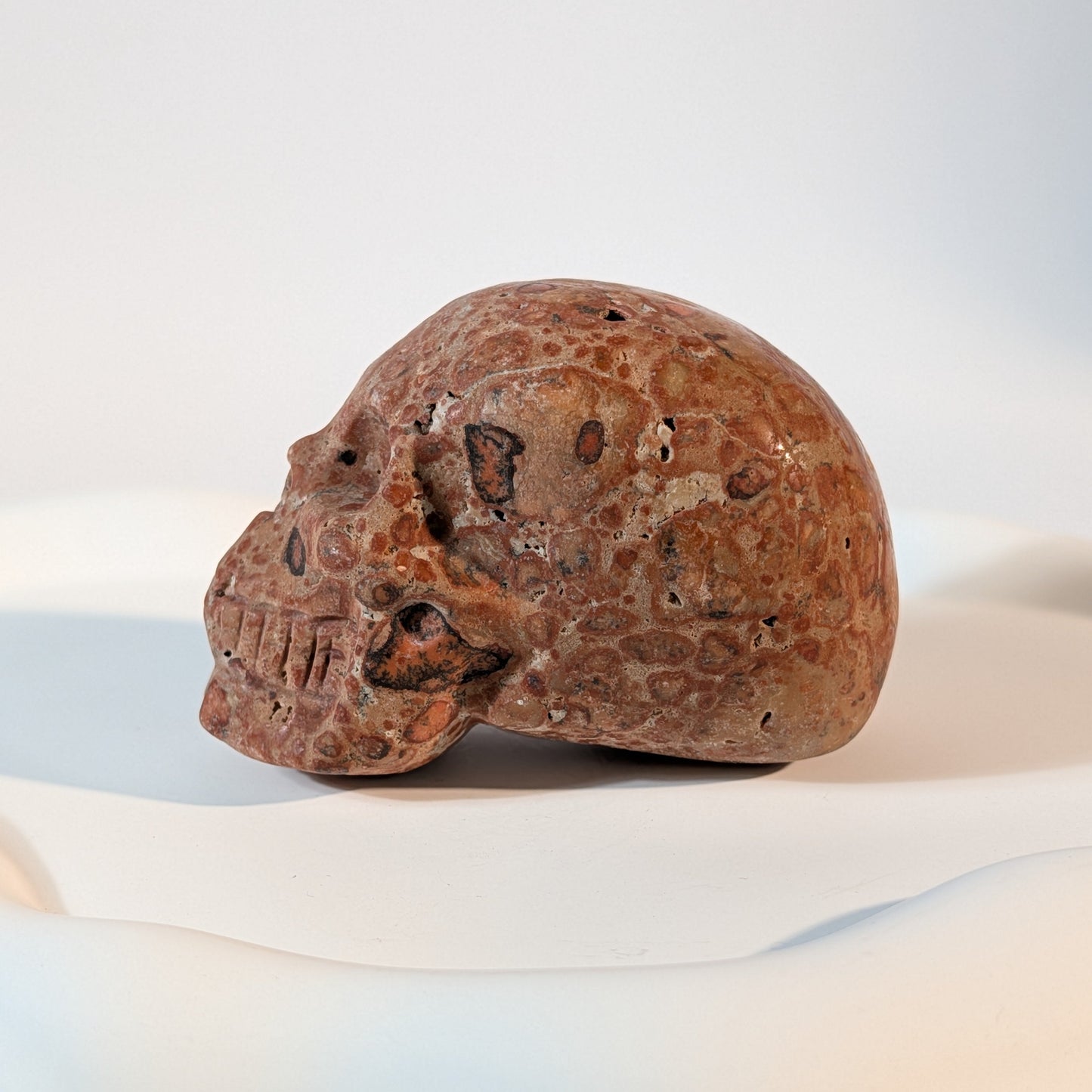 Massiver Kristallschädel Sidahan aus Rhyolith mit blutroter und rostbrauner, von Kratern und dunklen Pocken durchzogener Gesteinsmatrix.