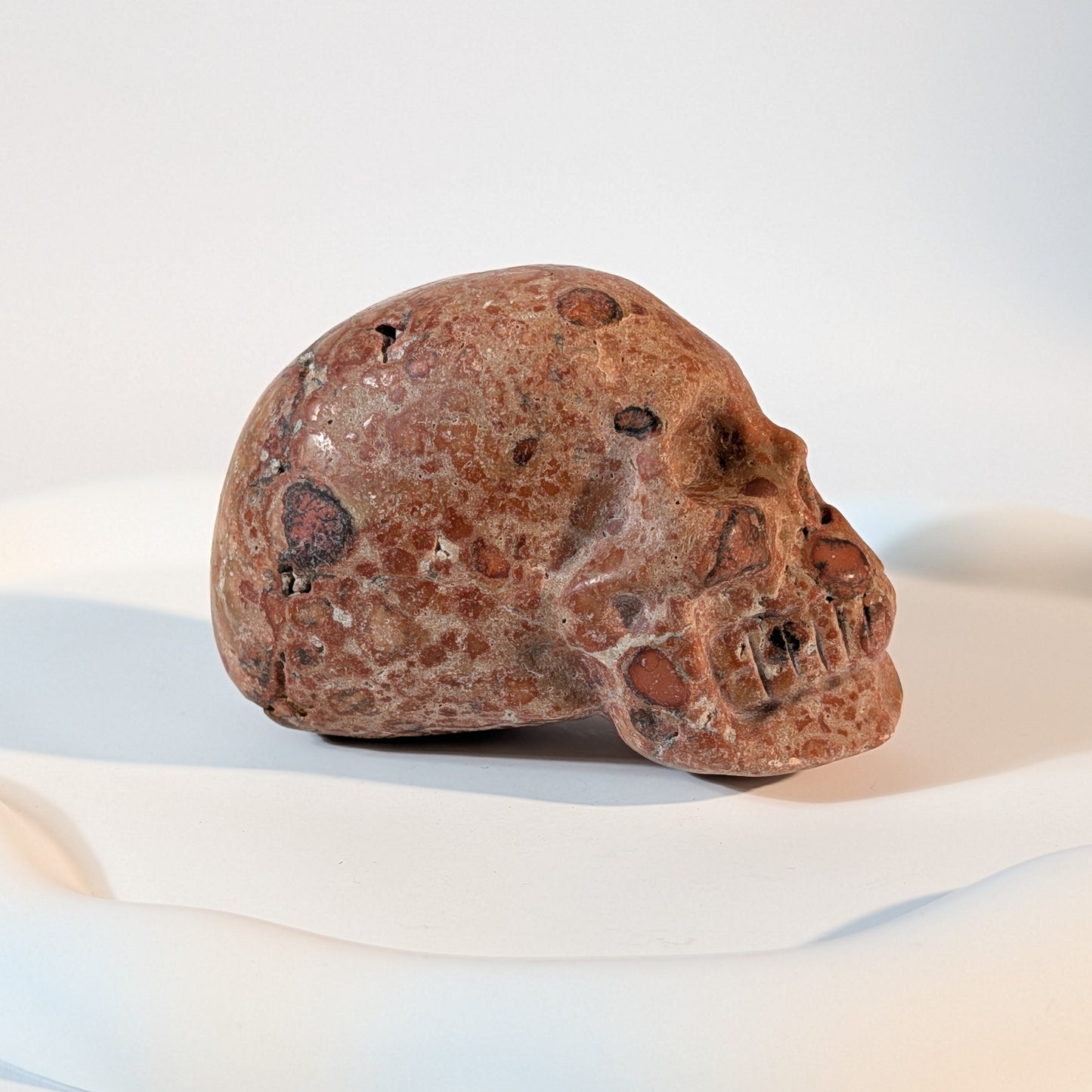 Massiver Kristallschädel Sidahan aus Rhyolith mit blutroter und rostbrauner, von Kratern und dunklen Pocken durchzogener Gesteinsmatrix.