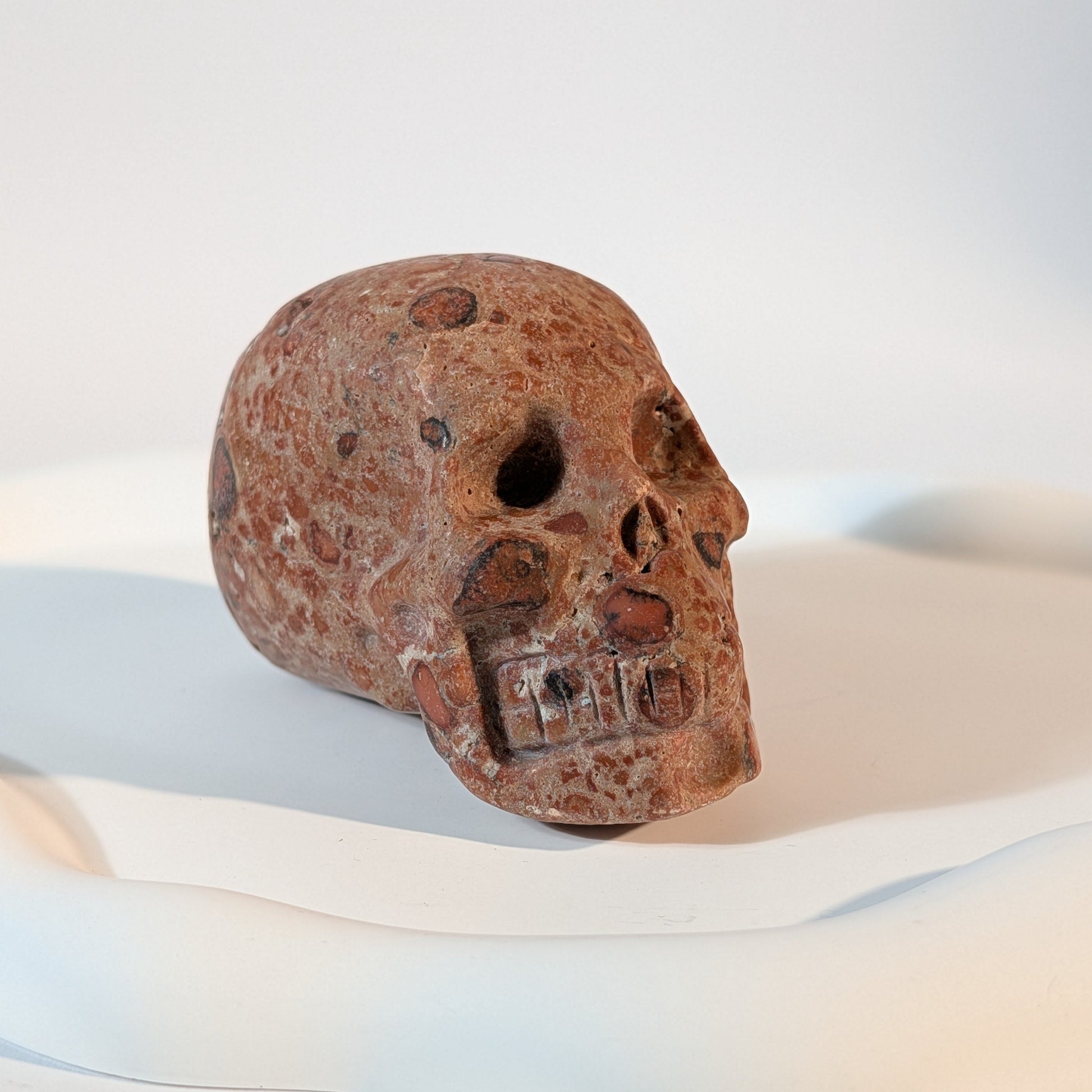 Massiver Kristallschädel Sidahan aus Rhyolith mit blutroter und rostbrauner, von Kratern und dunklen Pocken durchzogener Gesteinsmatrix.