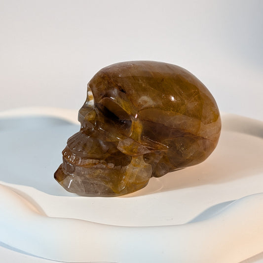 Massiver, bernsteinfarbener Kristallschädel Muirne aus Quarz mit tiefen, dunklen Rissen und rostigen Eiseneinschlüssen.