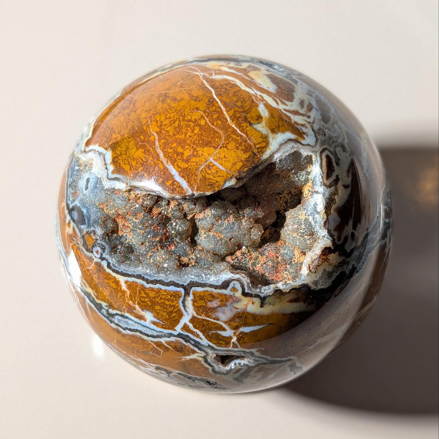 Polierte Drusenachat Kugel in Nahaufnahme mit offener Kristall-Geode und goldgelber Bänderung