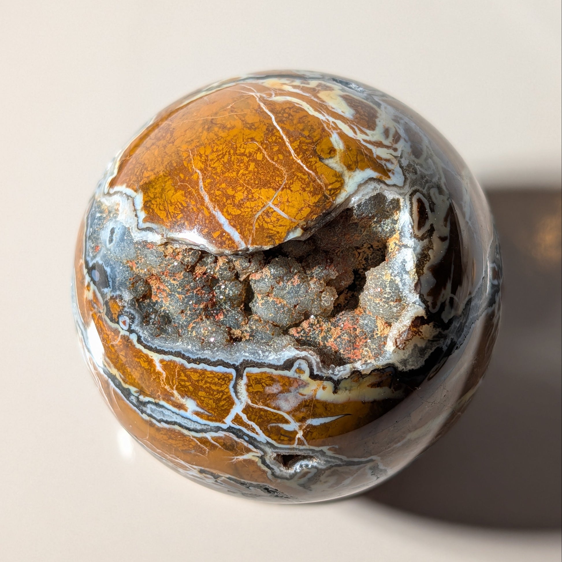 Polierte Drusenachat Kugel in Nahaufnahme mit offener Kristall-Geode und goldgelber Bänderung
