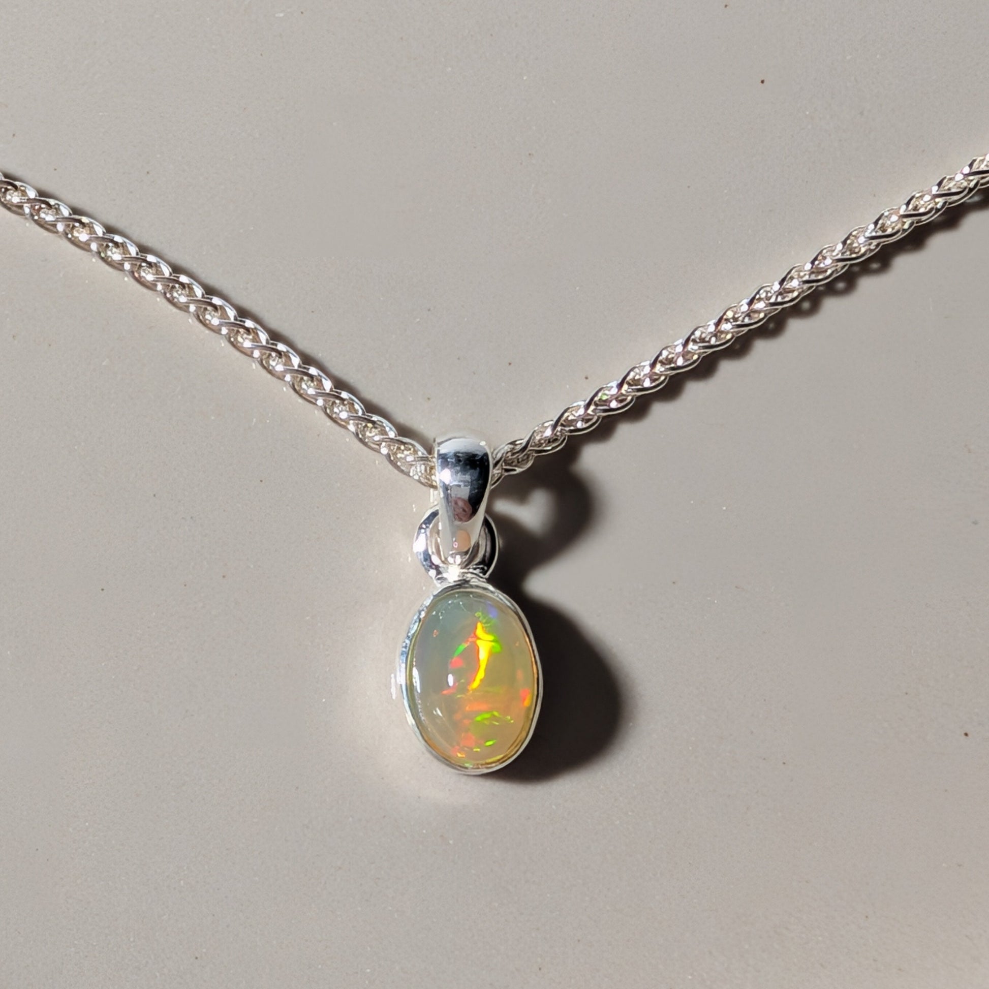 Polierter ovaler Opal Anhänger mit leuchtendem Farbspiel in einer schlichten 925er Silberfassung an einer Silberkette, energetisch aufgeladen von Temple of Desire